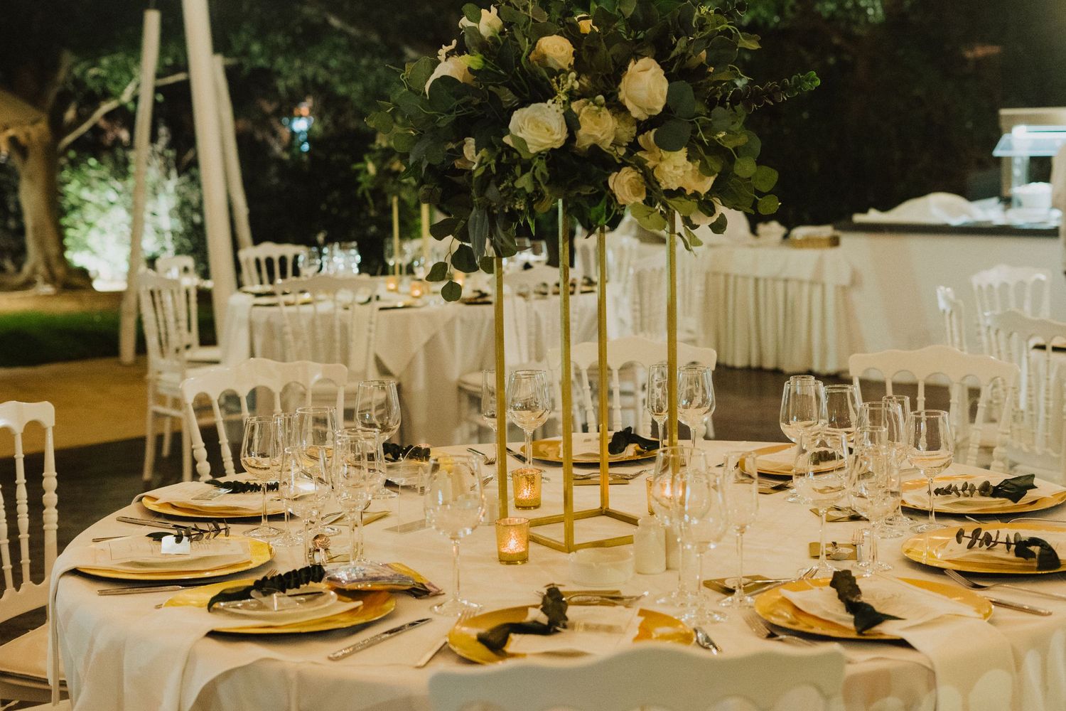 Elegant wedding reception table with white linens, gold centerpiece stands, and white floral arrangements.