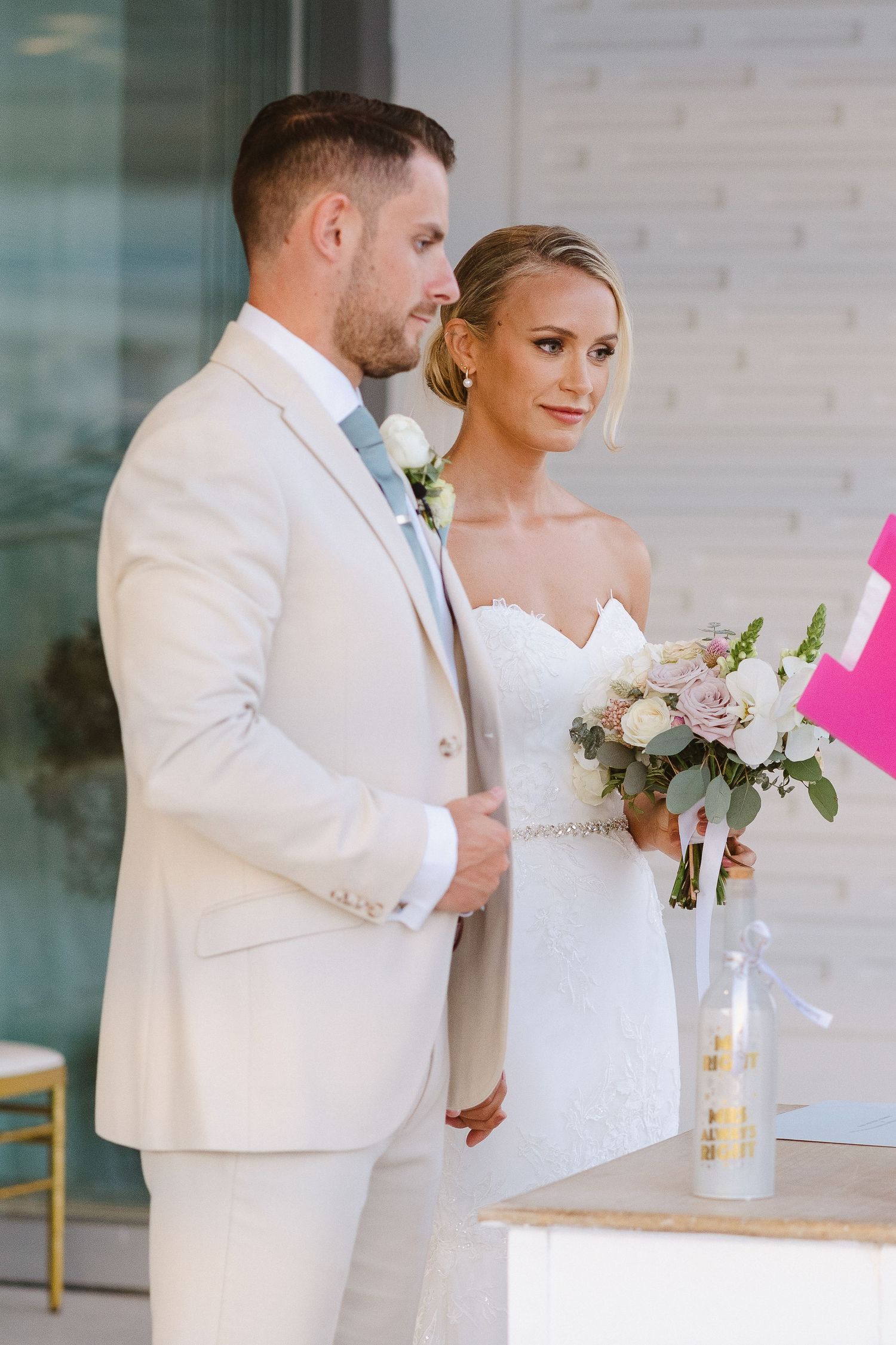 Elegant couple in white attire standing together during indoor wedding ceremony.