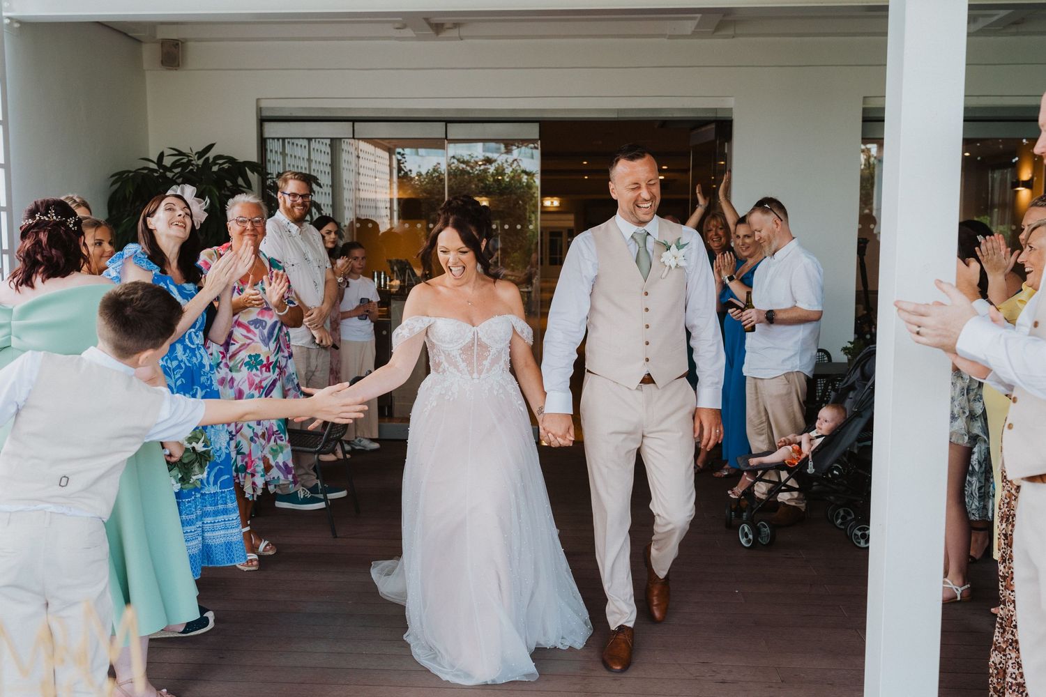 A newlywed couple exits their wedding ceremony as guests celebrate in a covered outdoor venue.