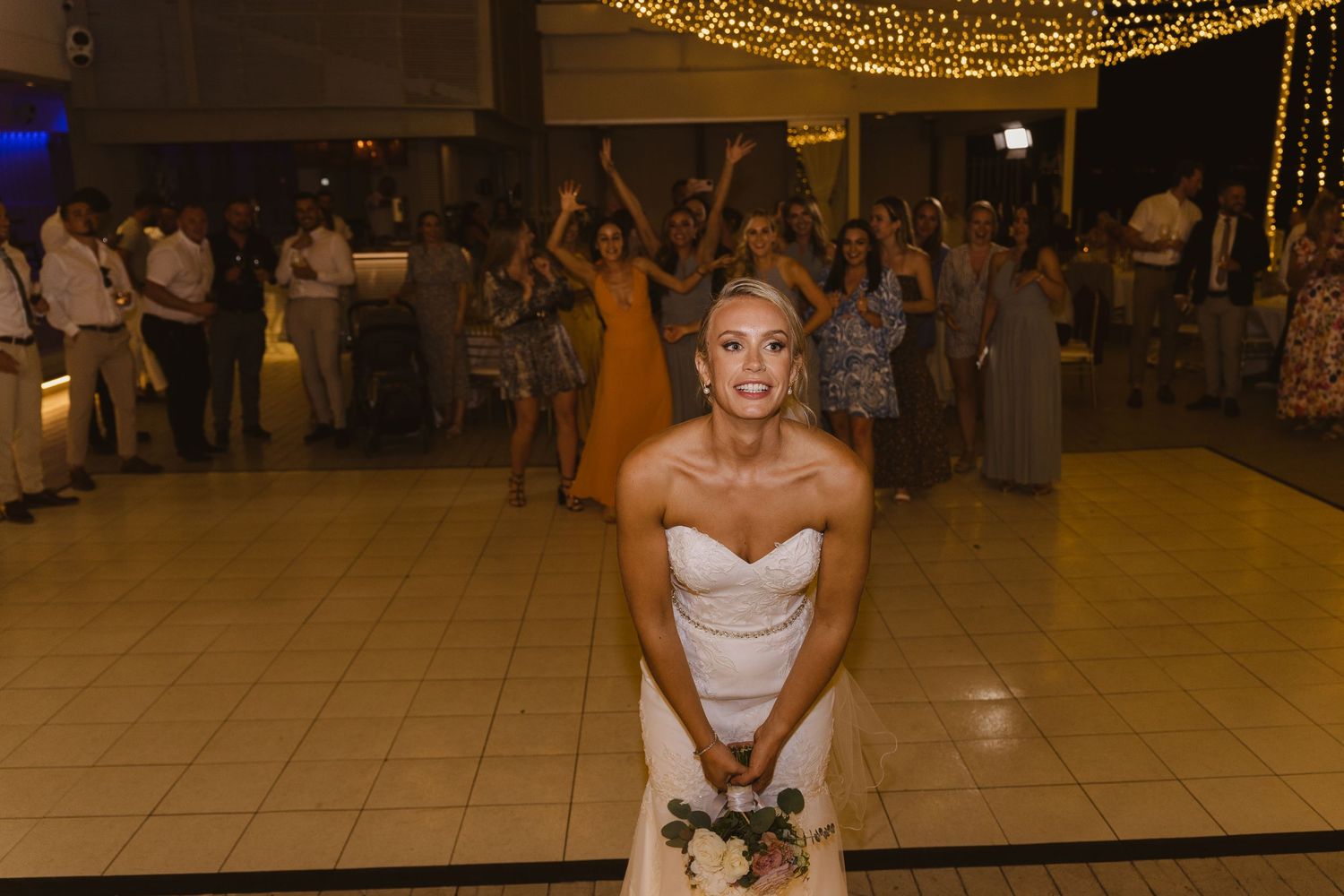 Bride prepares to toss her bouquet at wedding reception under glowing string lights.