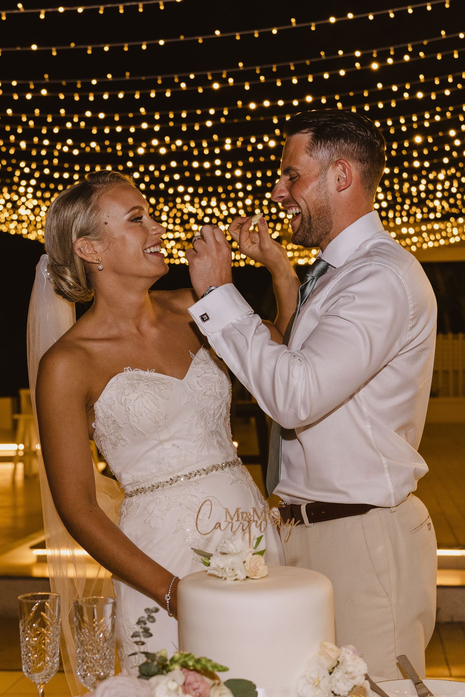 Couple enjoys cake tasting moment under a stunning ceiling of fairy lights at reception.