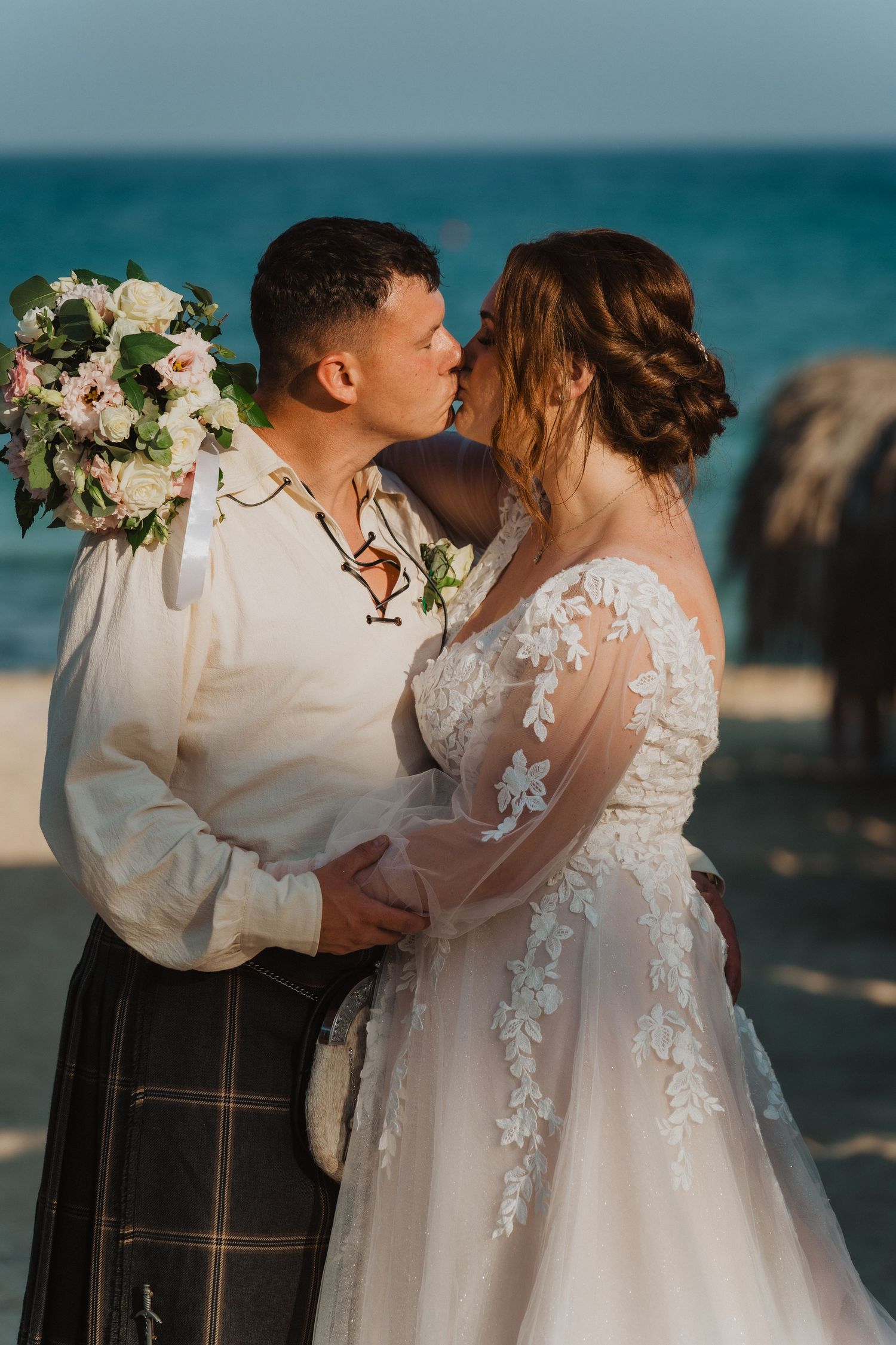Intimate beach wedding moment with traditional Scottish attire and lace wedding gown.