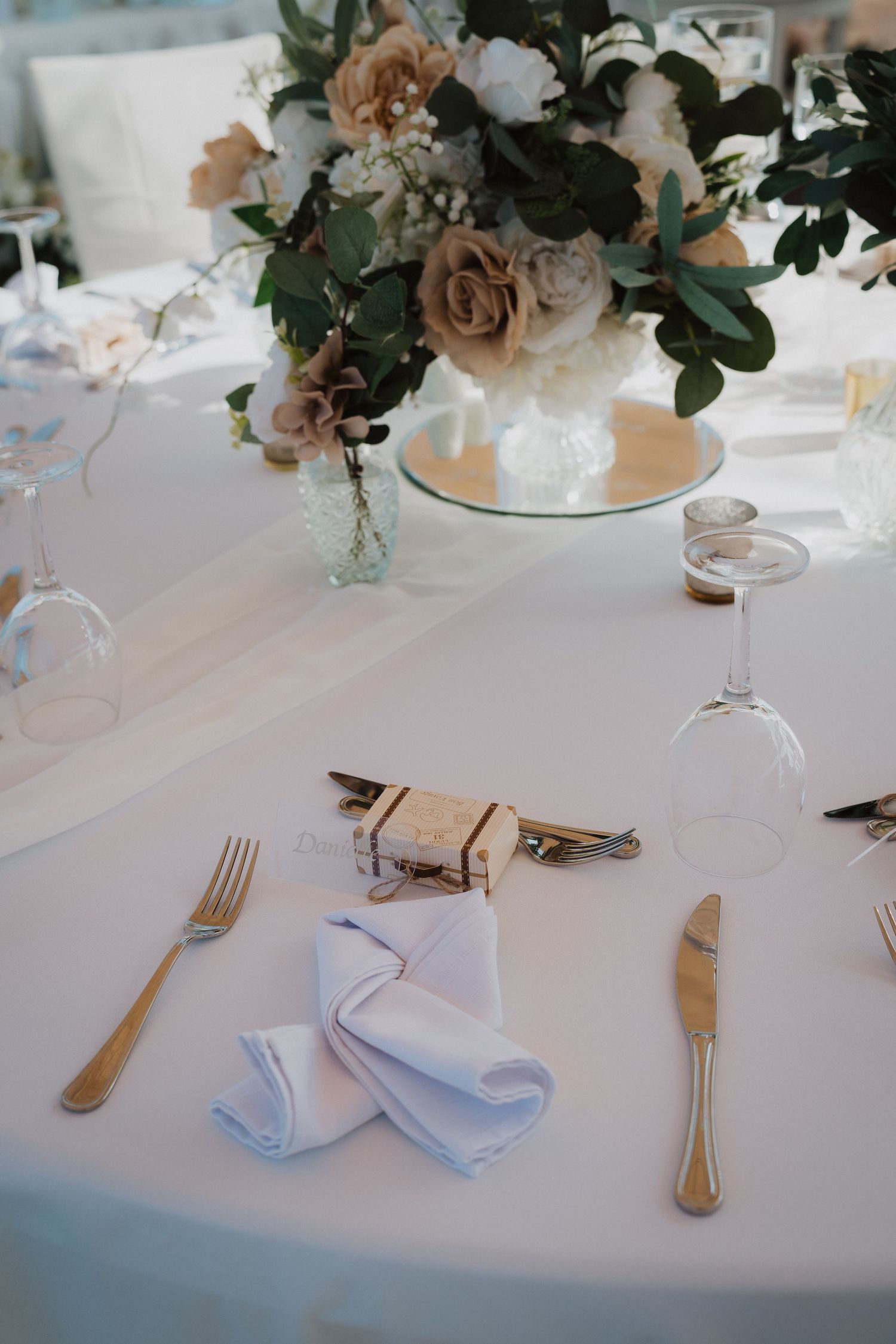 Lush floral arrangements with peach roses and greenery on mirrored wedding reception tables.