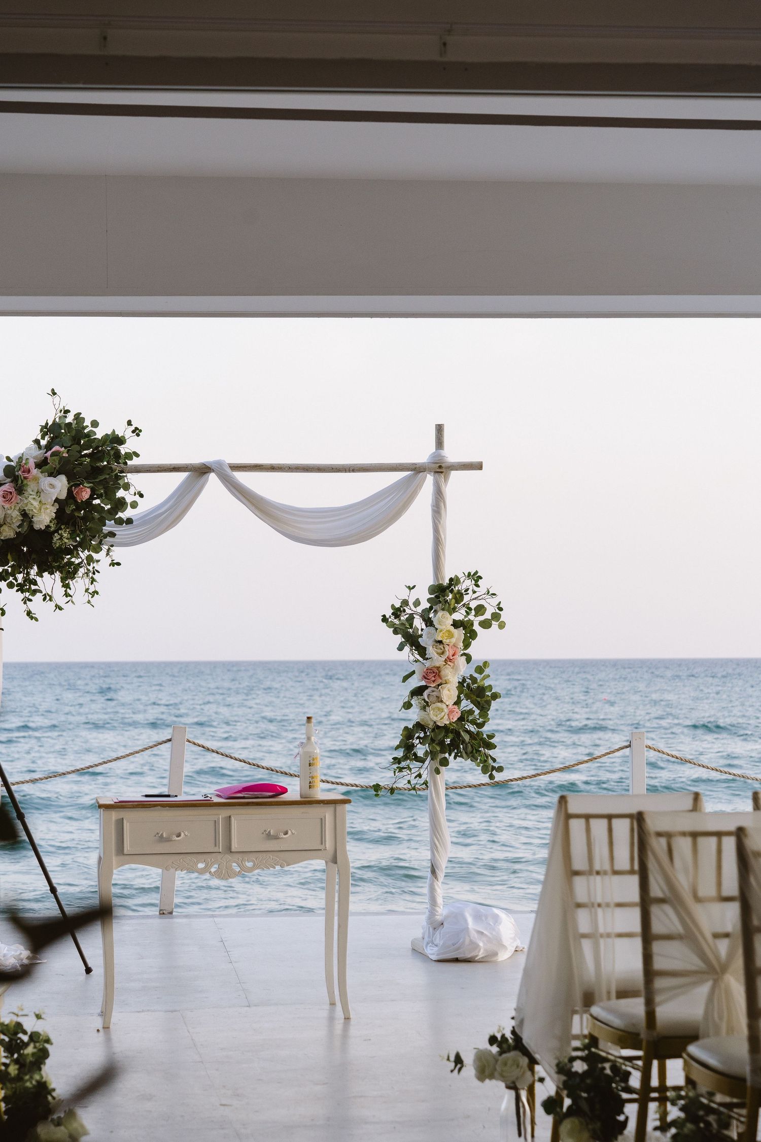 Seaside wedding ceremony altar with white draping and floral arrangements overlooking the ocean.