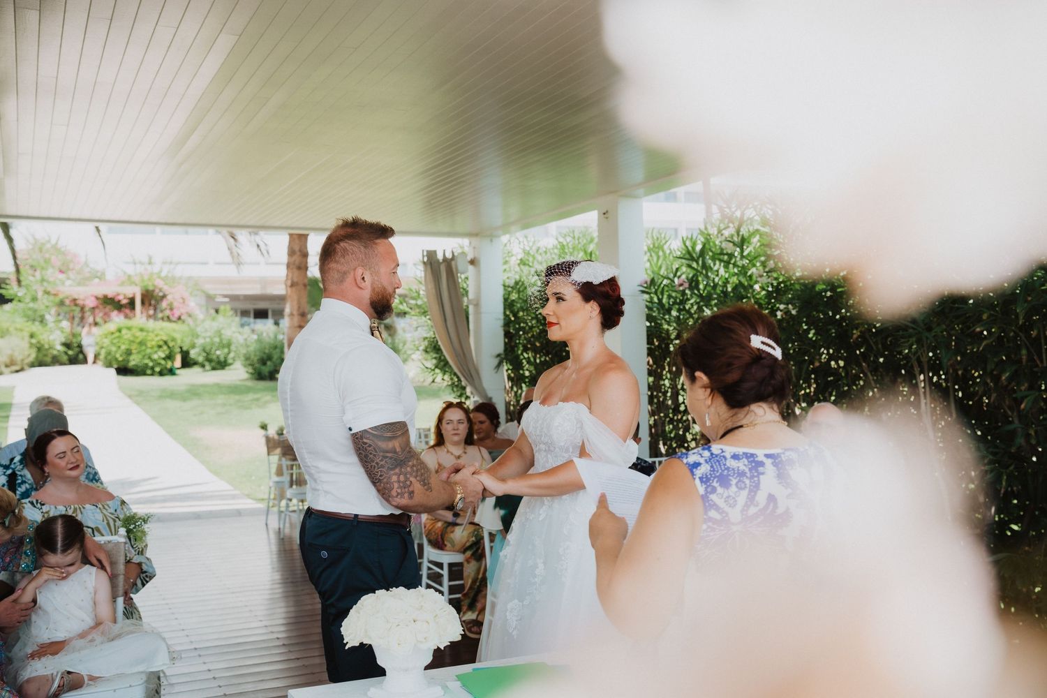 An intimate outdoor wedding ceremony on a covered porch with floral decorations.