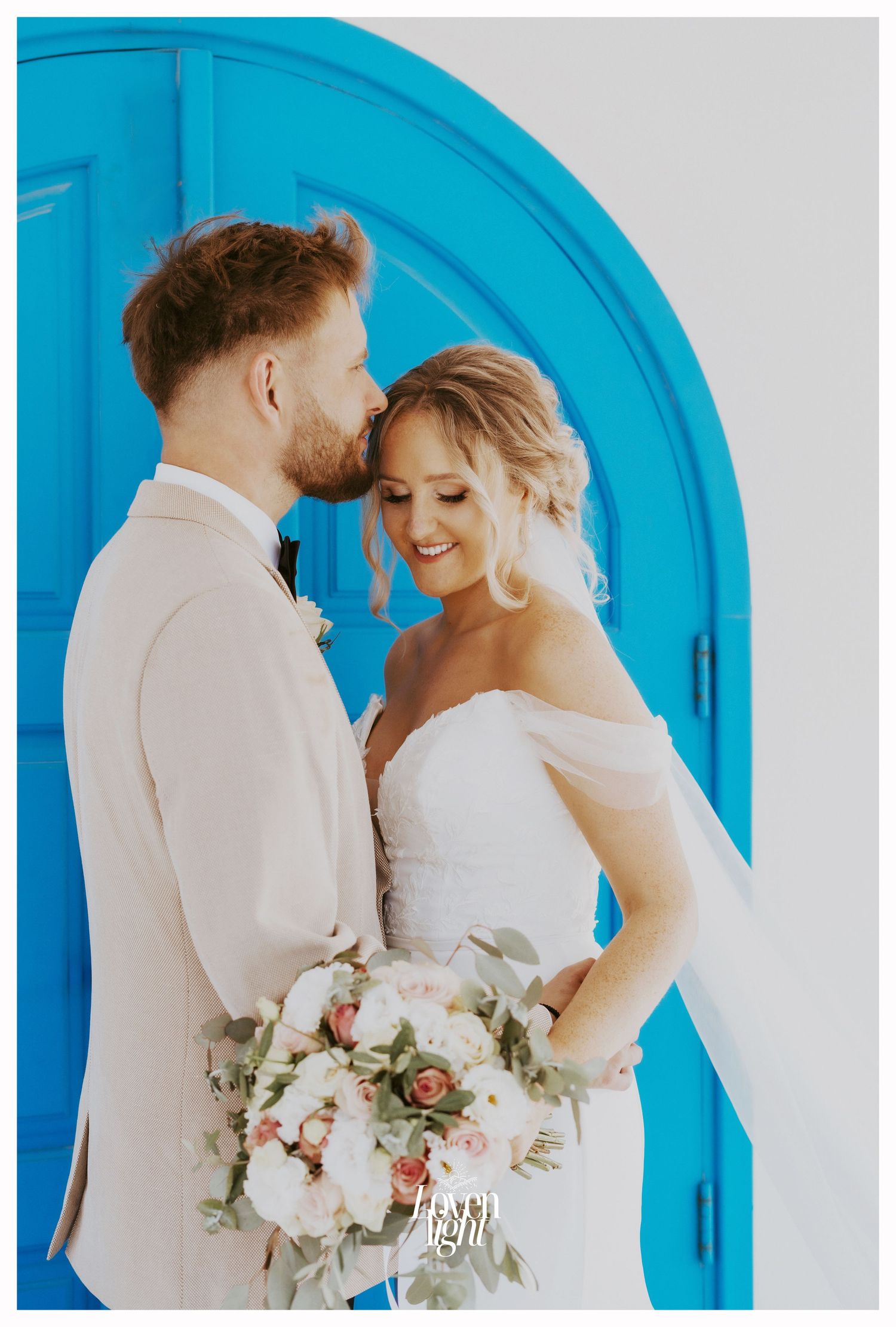 Romantic wedding portrait with couple sharing intimate moment against bright blue archway.