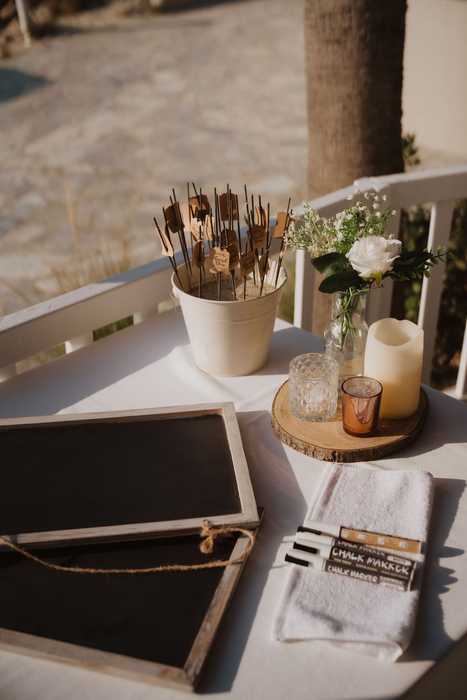Wedding guest book table with chalkboard, candles, and floral decor in outdoor setting.