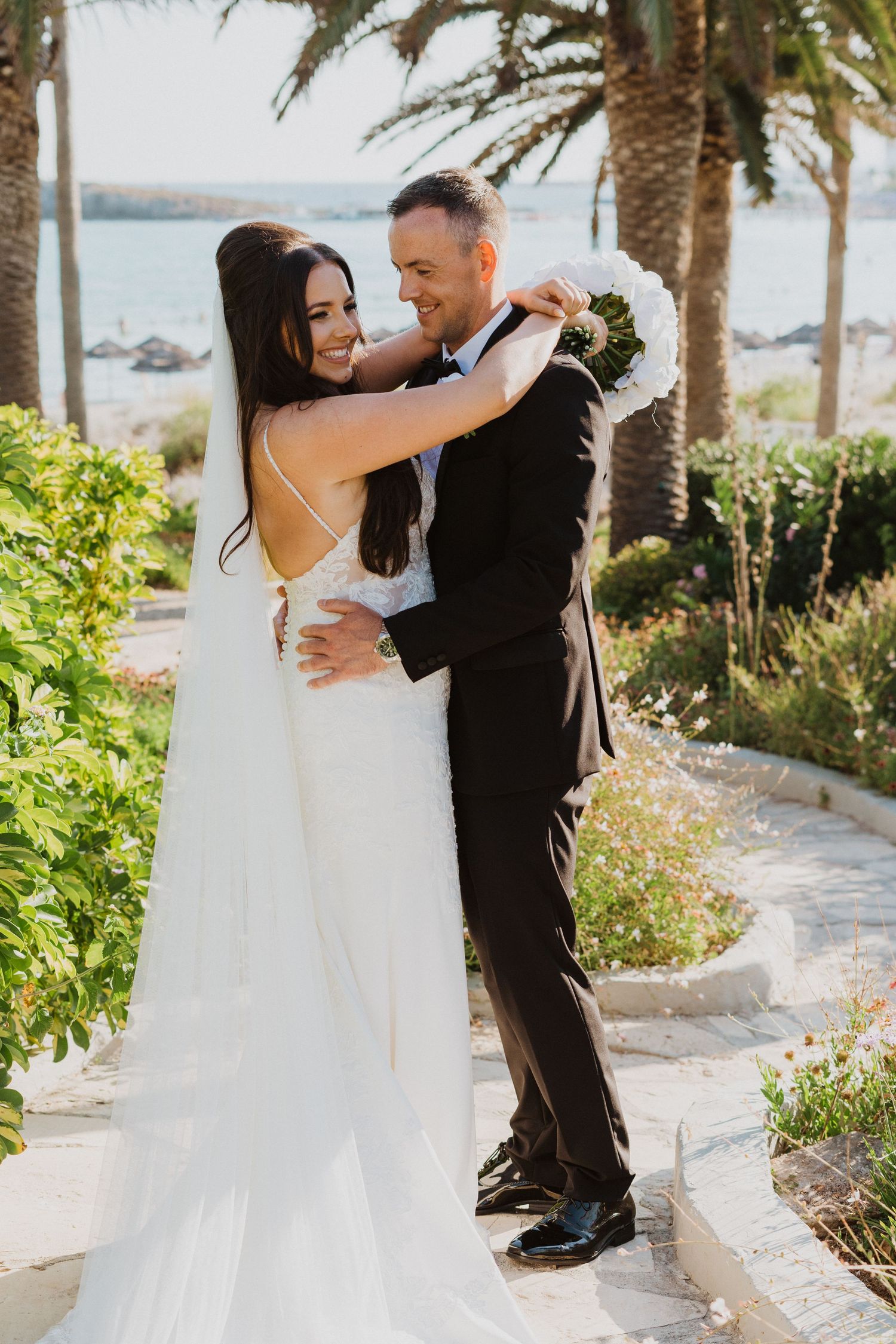 A tender wedding moment captured in a tropical garden setting with palm trees.