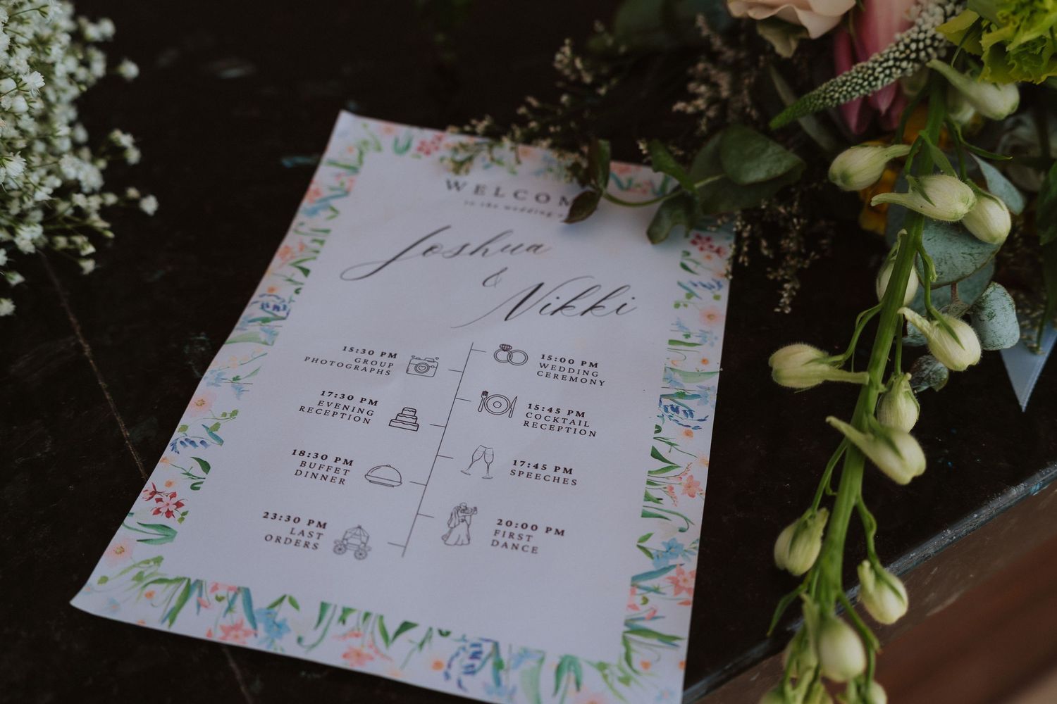 A wedding timeline schedule card with floral border design lies next to eucalyptus branches and white flowers.