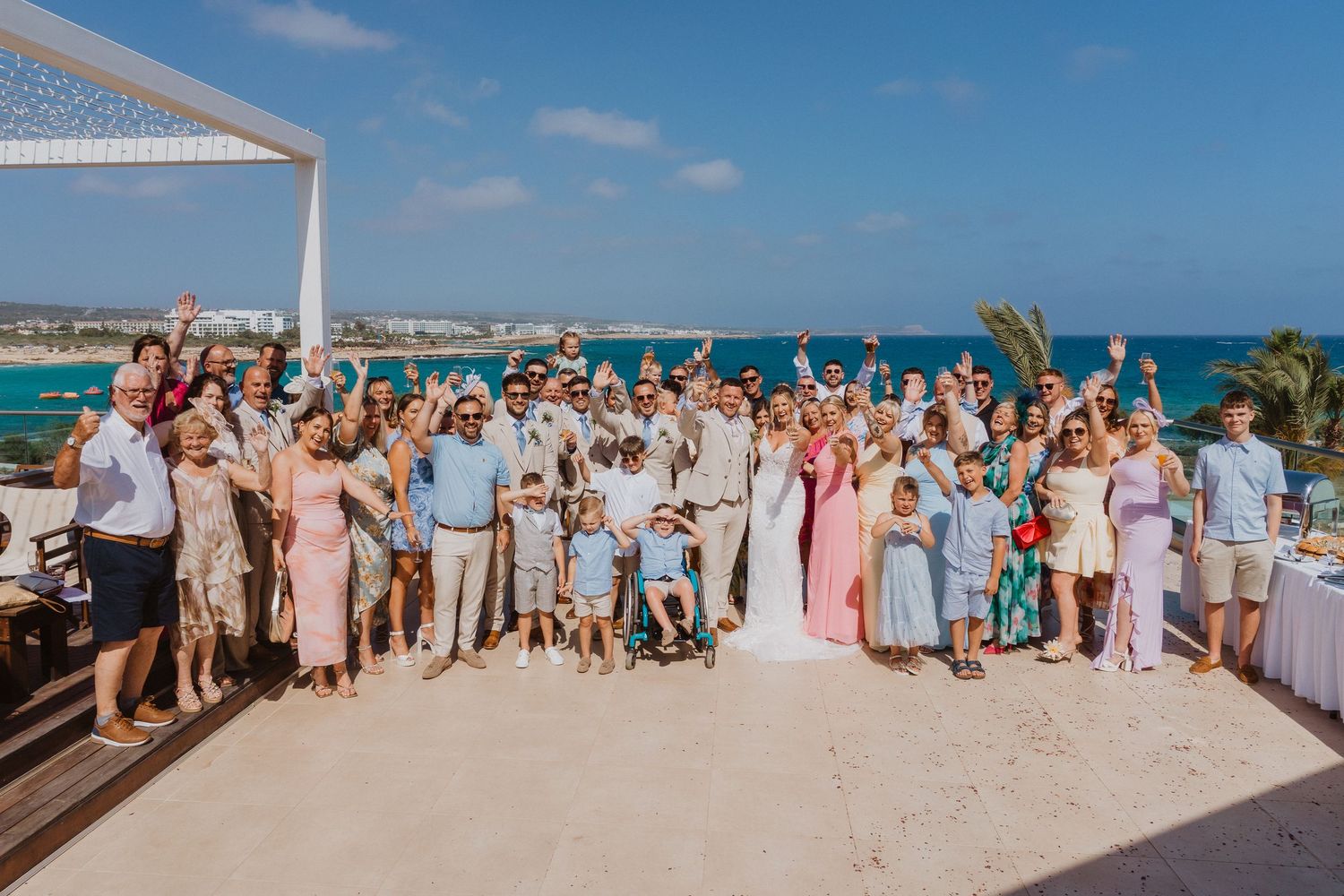 Wedding party gathered on a sunny beach with turquoise waters and white sand in the background.