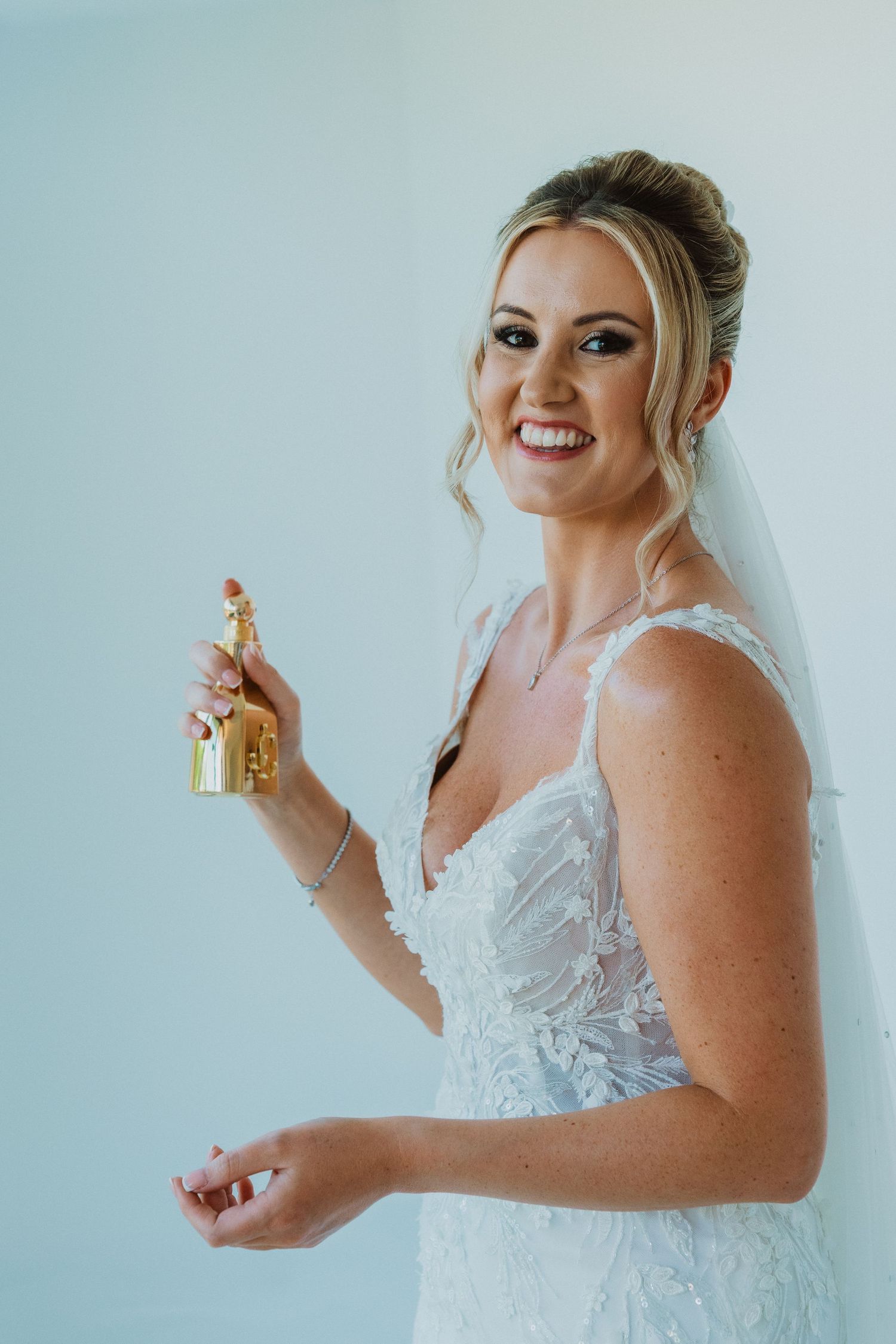 A bride in a white lace wedding dress sprays perfume while getting ready for her special day.