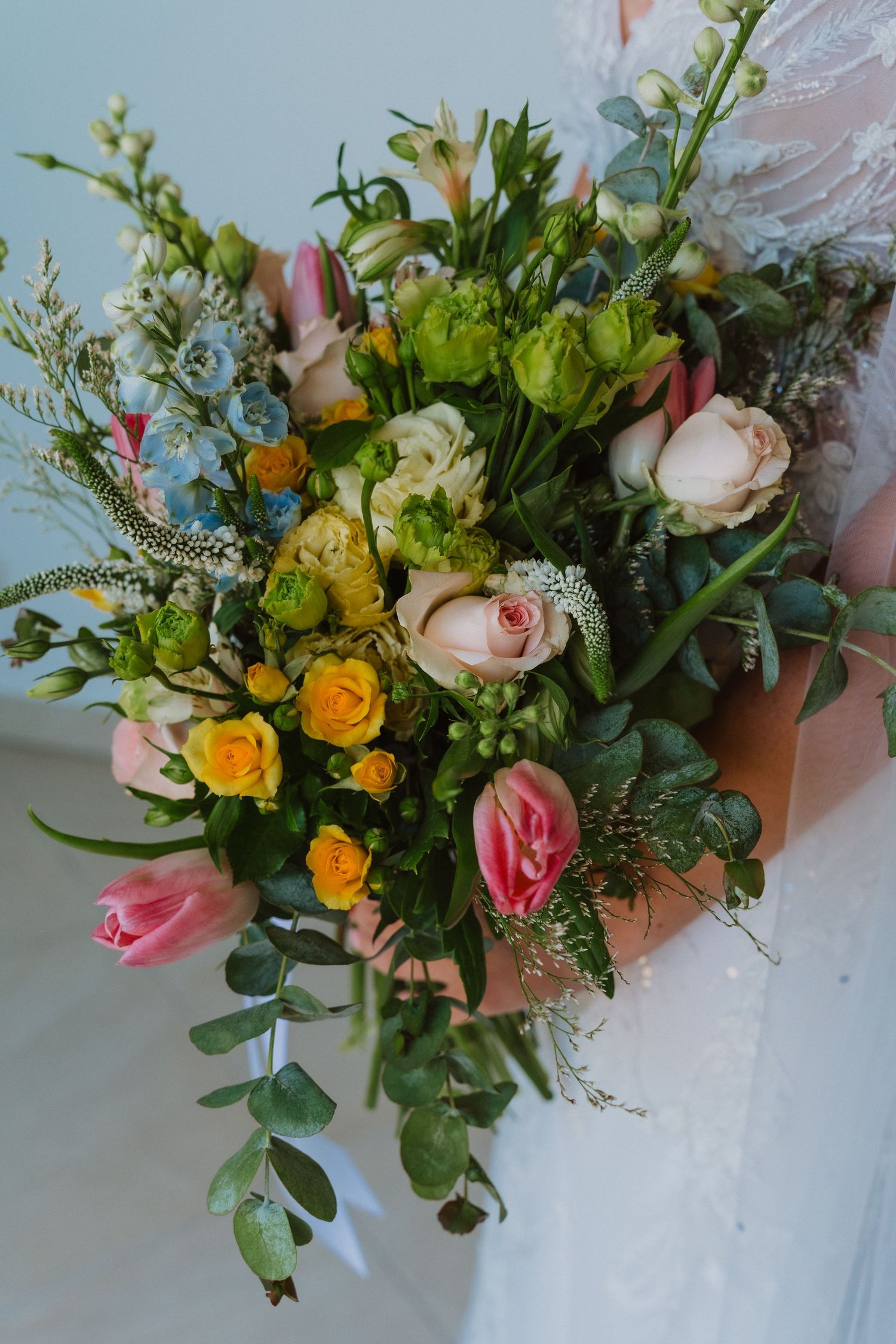 A stunning bridal bouquet features pink and yellow roses with mixed greenery and delicate white blooms.