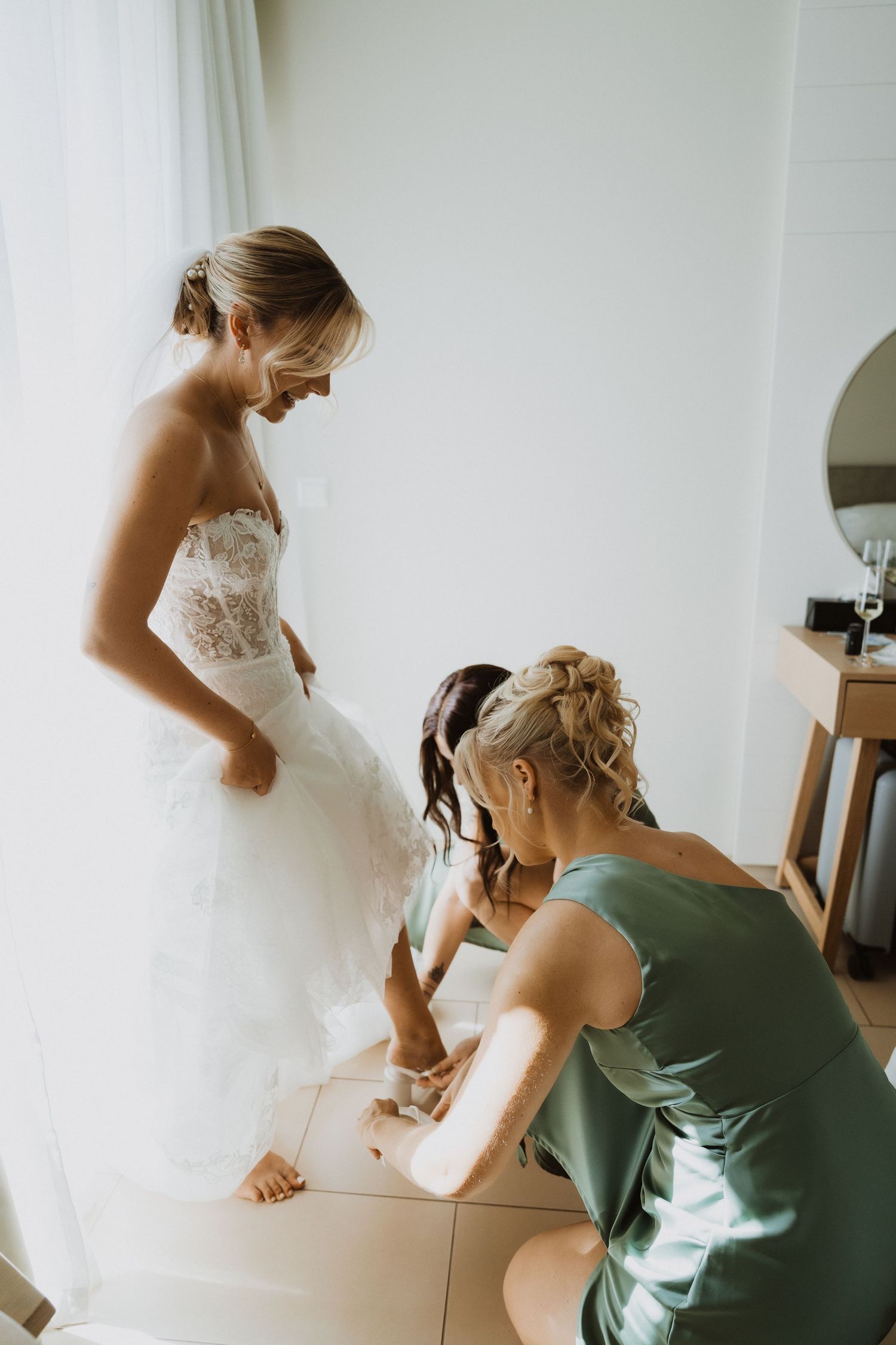 Wedding dress preparation with helpers in a bright room.