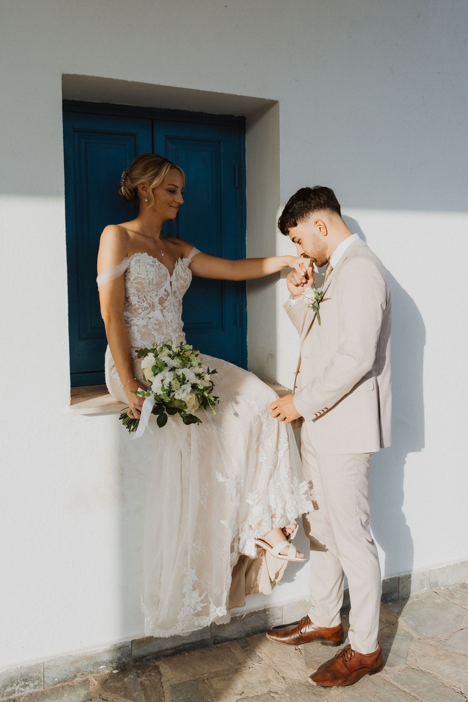Wedding couple interacts playfully near blue doorway in Mediterranean architecture.