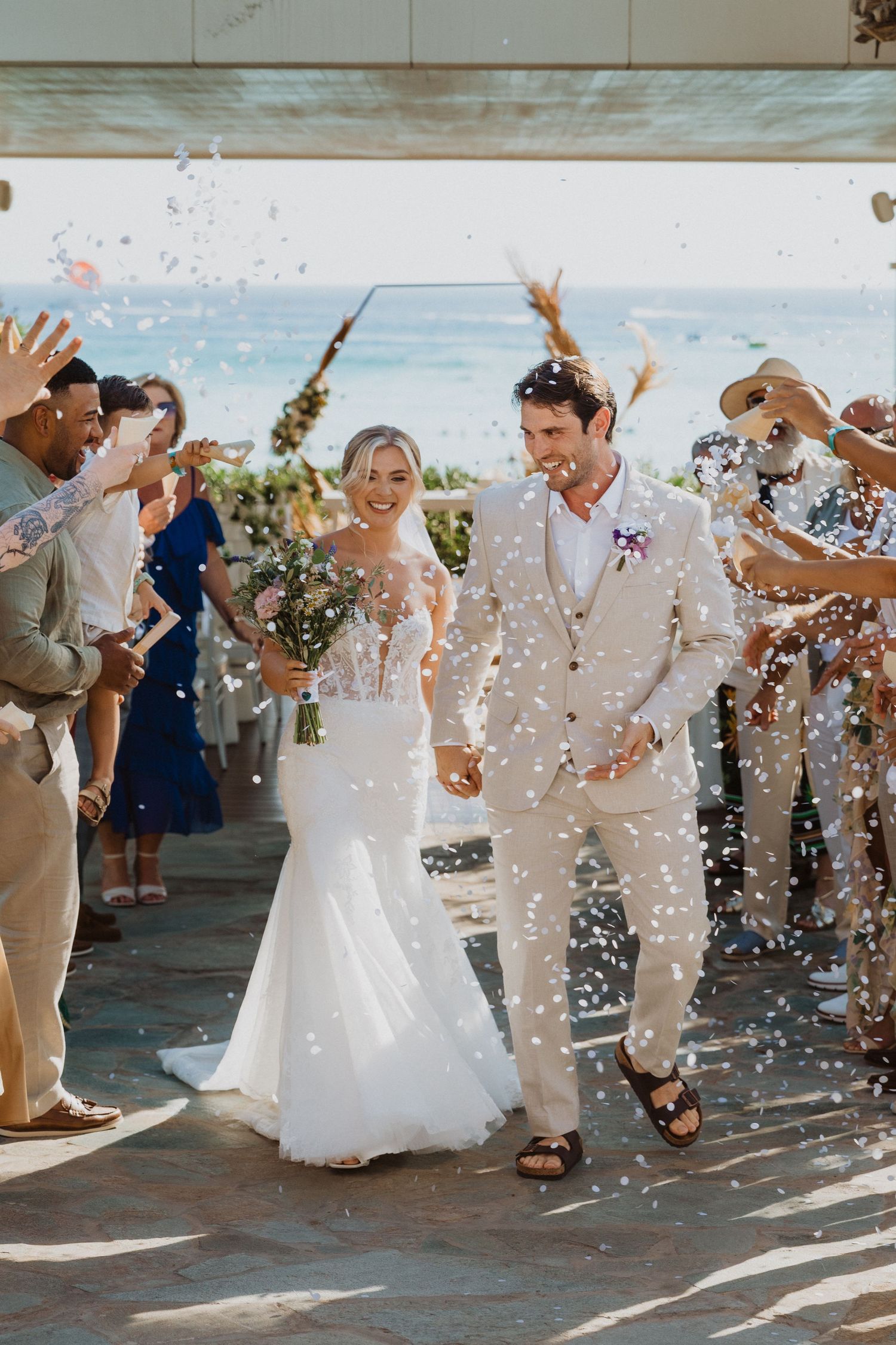 Joyful wedding exit with confetti shower and cheering guests at outdoor venue.