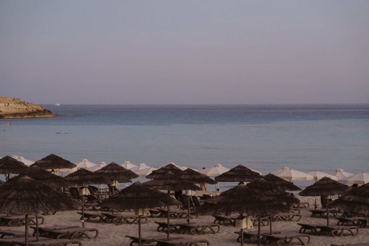 Beach scene at dusk with rows of umbrellas and lounge chairs along the shoreline.
