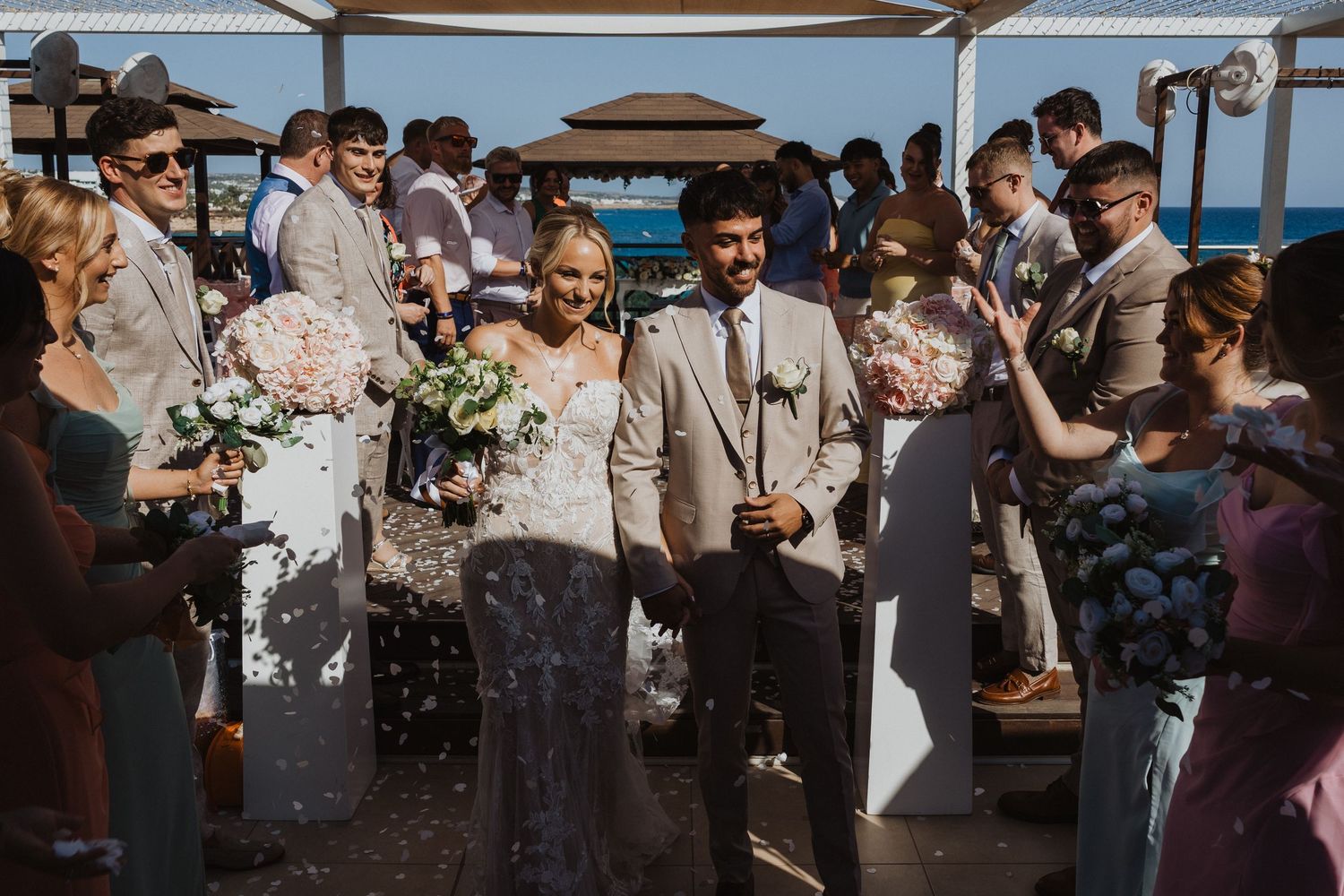 Wedding guests celebrating and throwing confetti at an outdoor ceremony by the ocean.