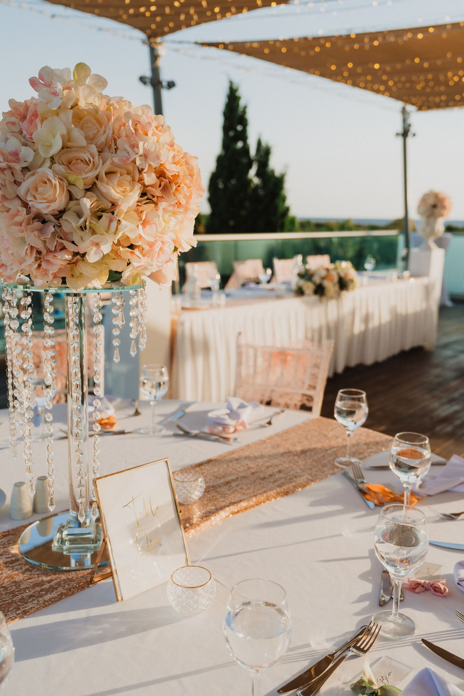 Elegant wedding reception tables with crystal centerpieces and peach floral arrangements under string lights.