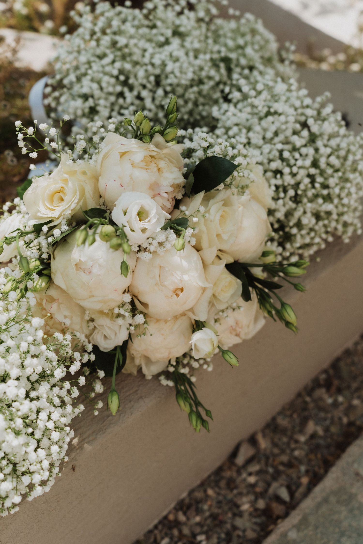 Elegant bridal bouquet of white peonies and baby's breath flowers resting on a wooden surface.