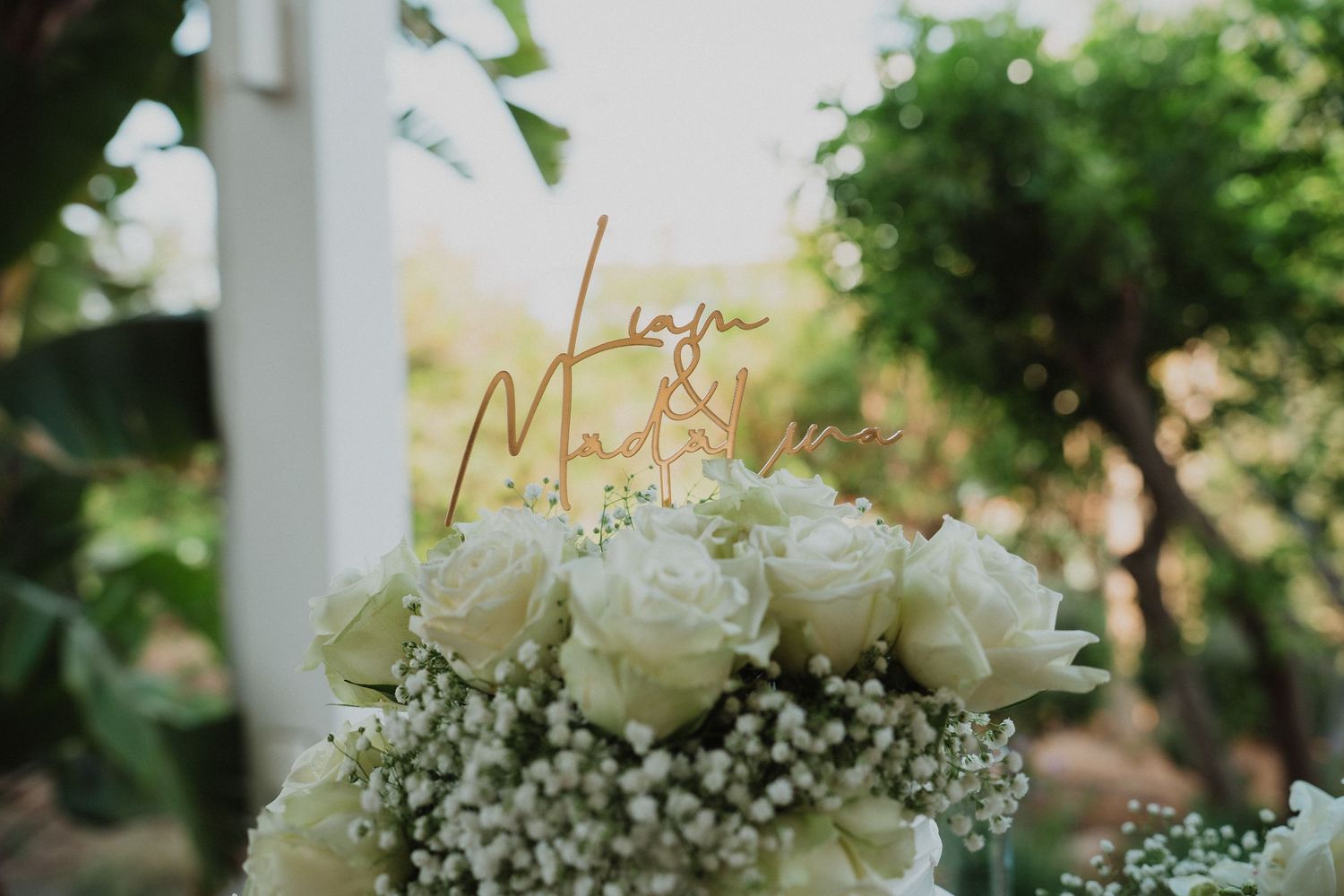 Close-up of white rose and baby's breath wedding cake topper with custom acrylic Liam and Madison sign.