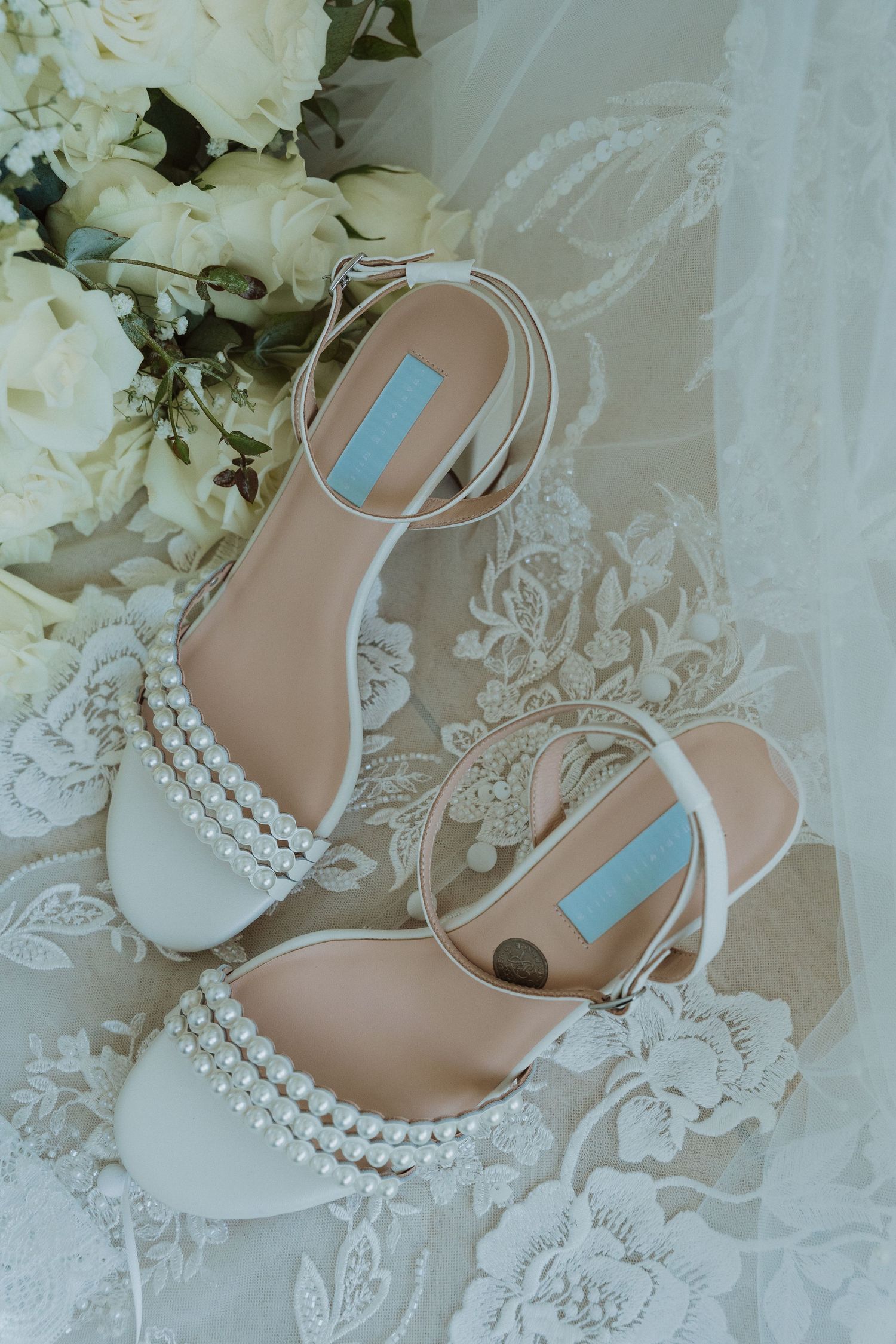 Elegant white pearl-embellished bridal shoes displayed with delicate lace and floral arrangements.