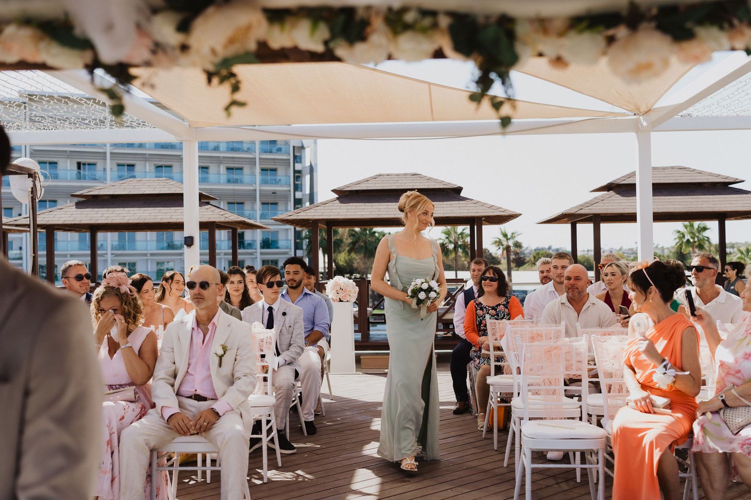 Wedding ceremony setup on a wooden deck with white chairs and covered pavilions.