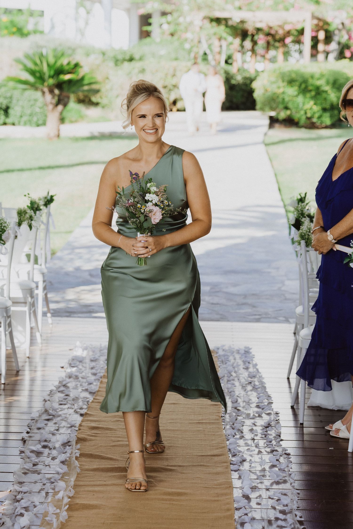 Bridesmaid in sage green dress poses on decorated outdoor walkway.