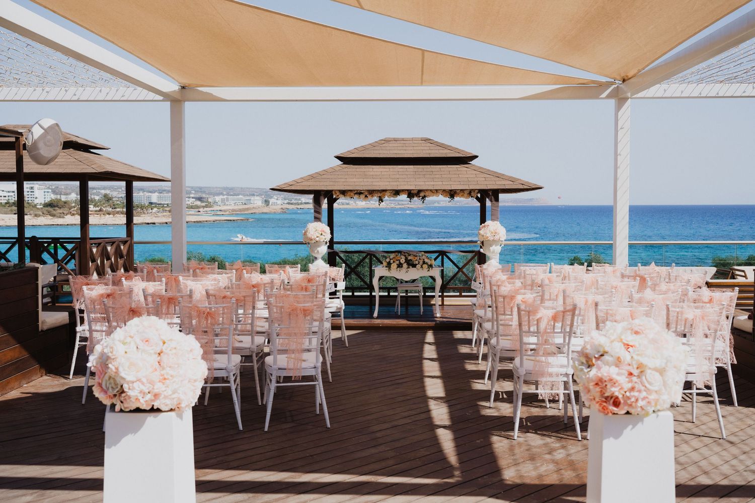 Elegant beachfront wedding ceremony setup with white chairs and peach decor overlooking the ocean.