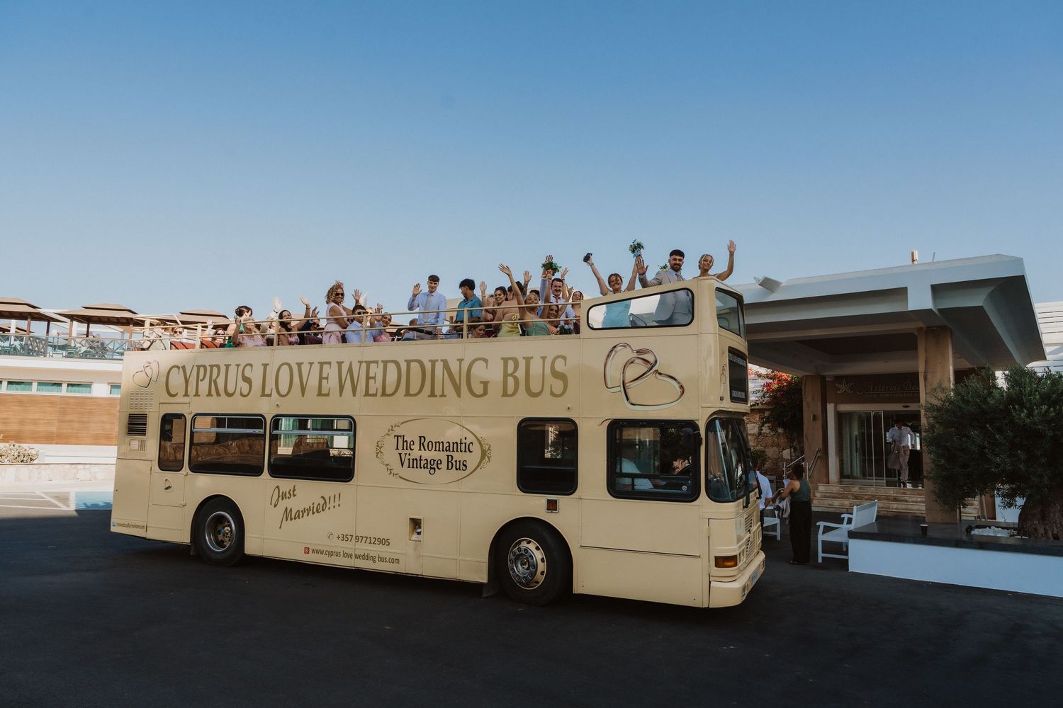 Wedding party celebrates atop a double-decker tour bus at sunset.