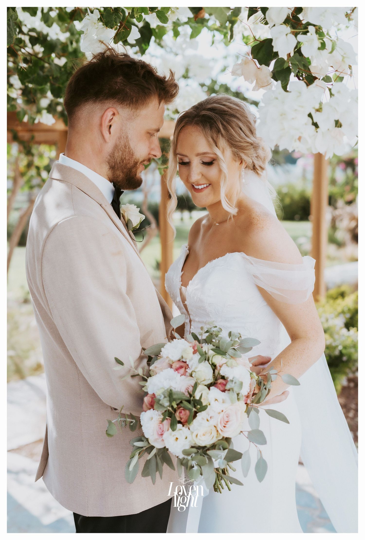 Intimate wedding portrait under flowering trees with a stunning floral bouquet.
