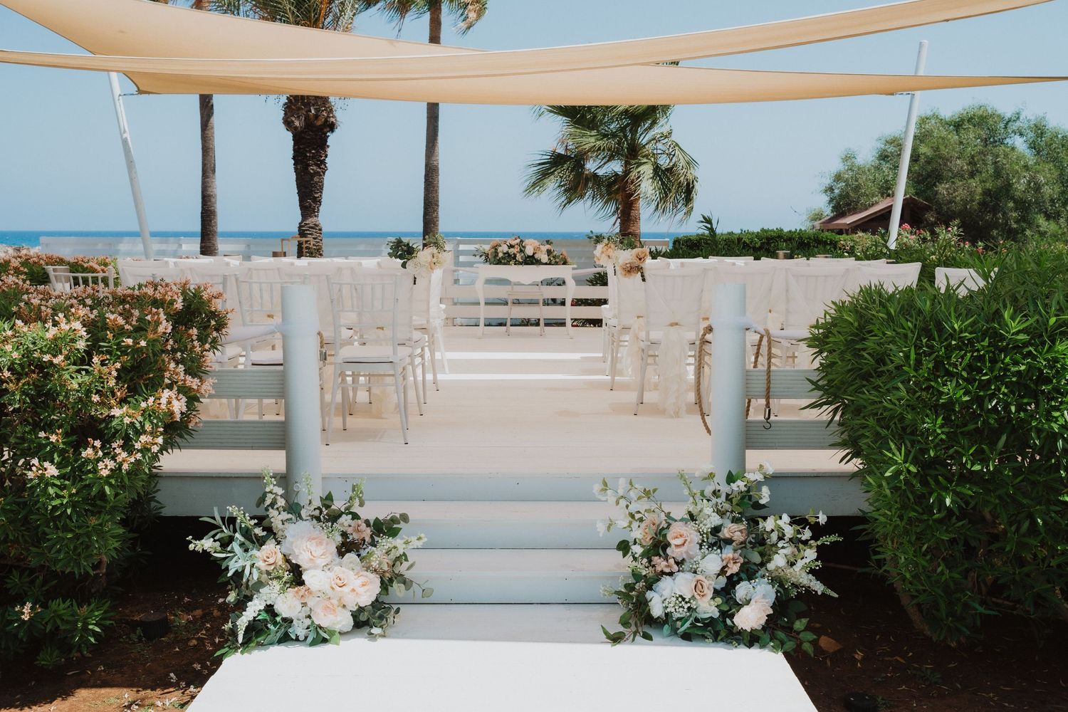 Outdoor beach wedding ceremony setup with white chairs and floral arrangements.
