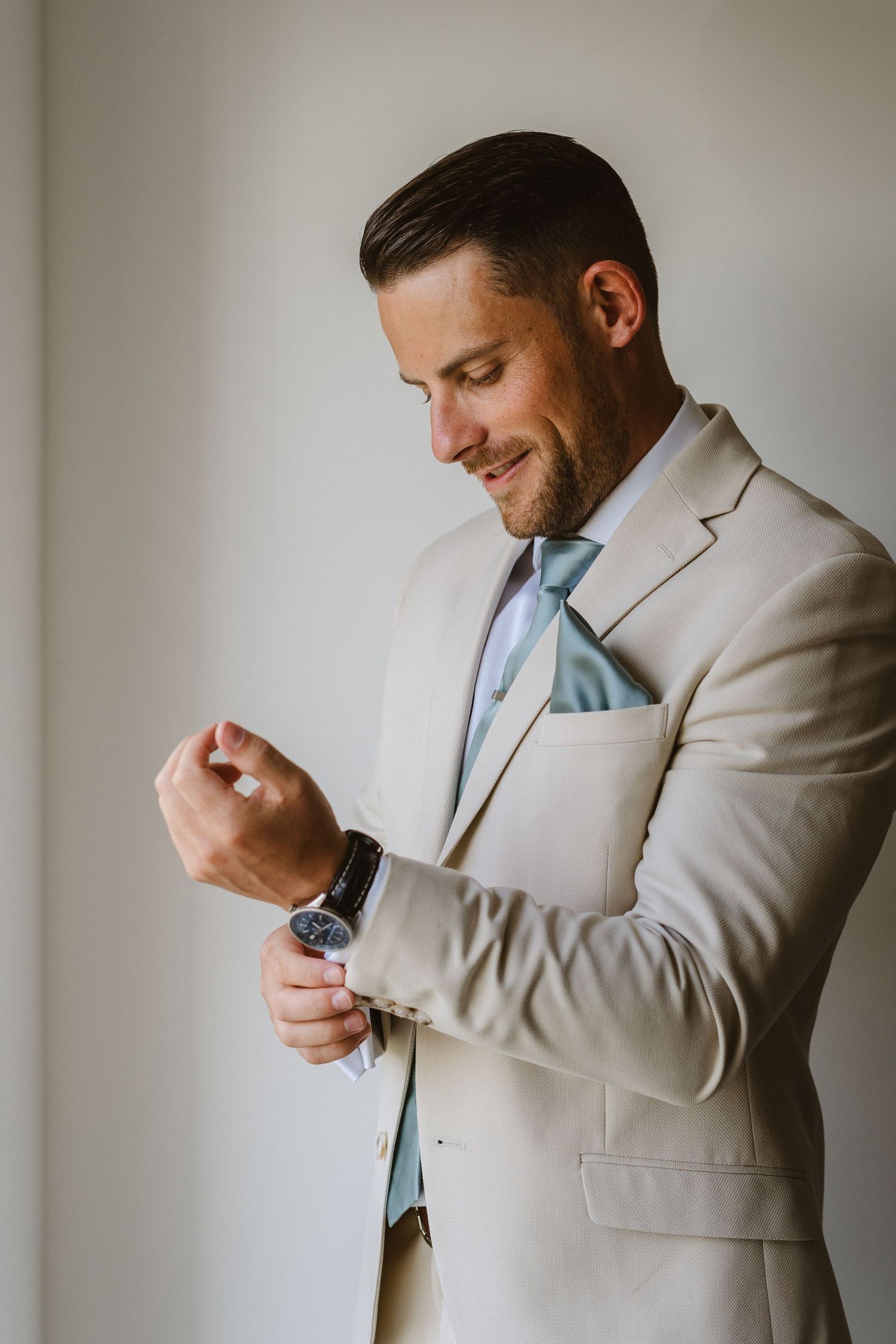 Professional portrait of someone in a light beige suit adjusting their watch.