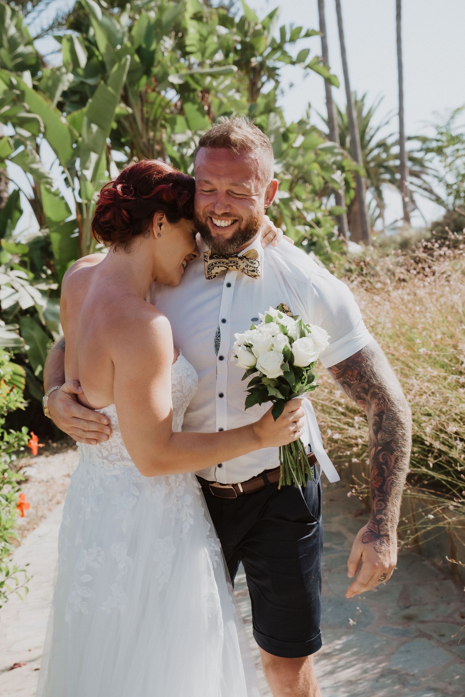 Candid moment of laughter between newlyweds in tropical garden setting.