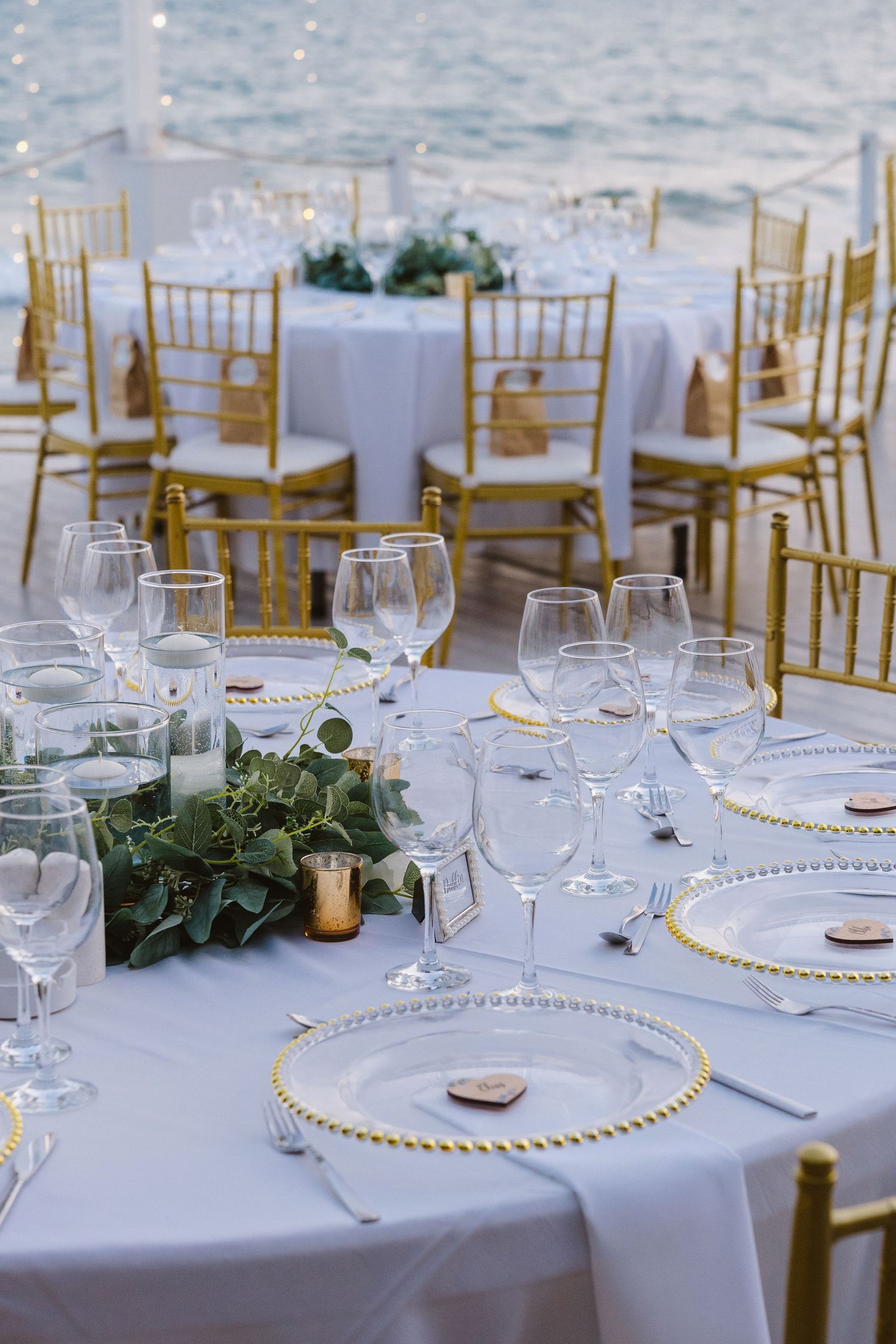 Wedding table setting with gold-rimmed charger plates, wine glasses and gold chiavari chairs.