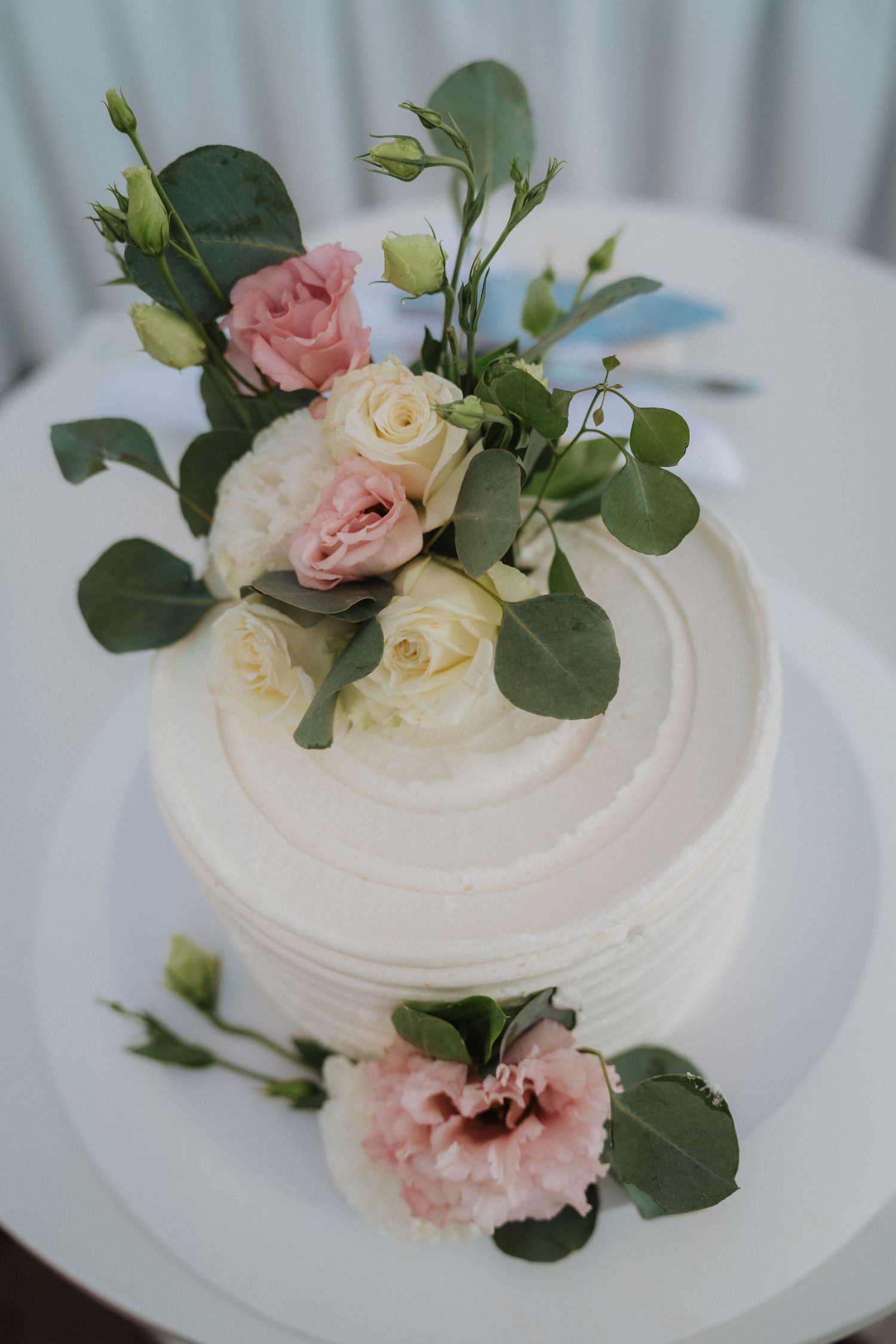 Close-up of white wedding cake topped with pink and cream roses and green foliage.