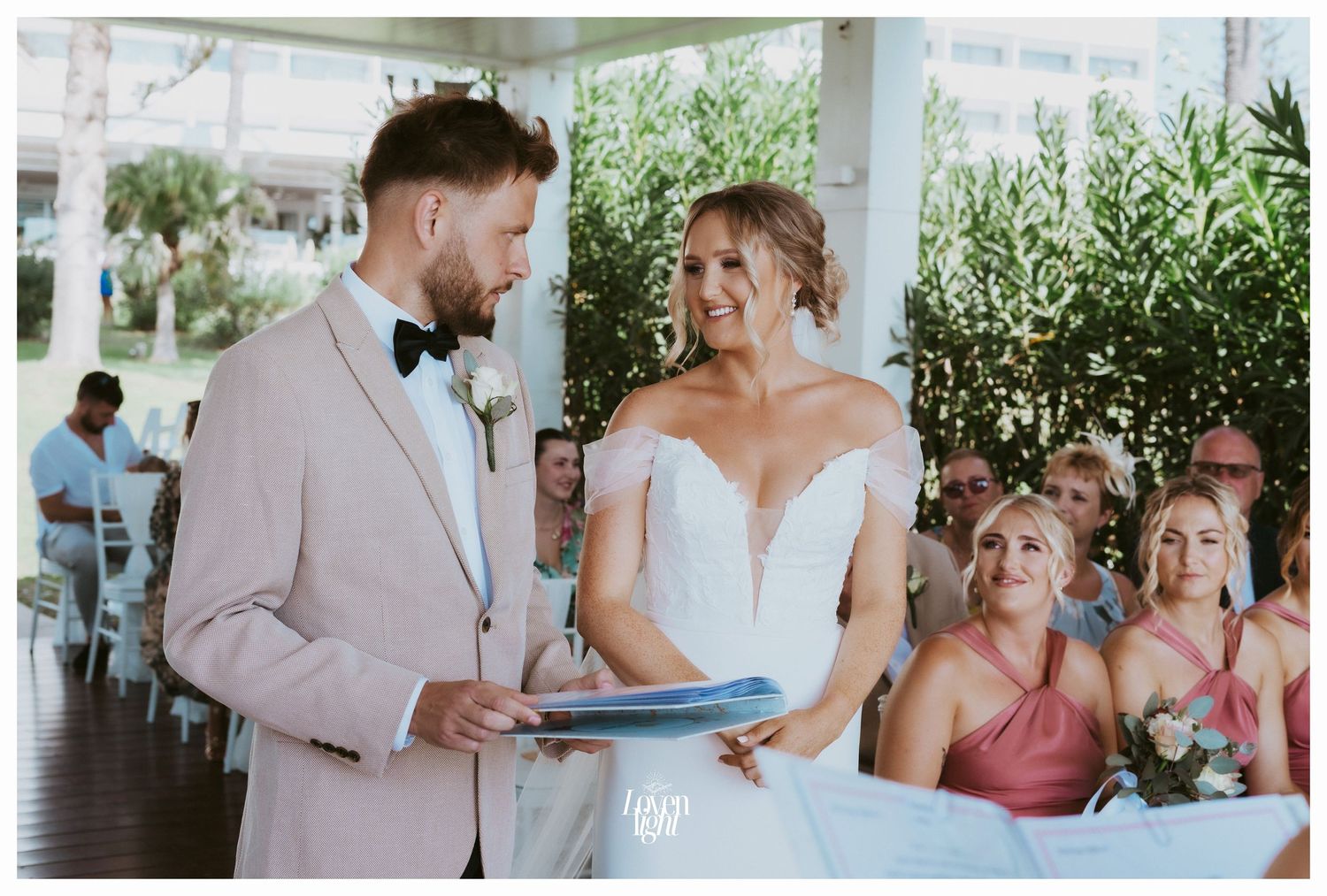 A wedding ceremony takes place on a covered patio with guests seated in white chairs.