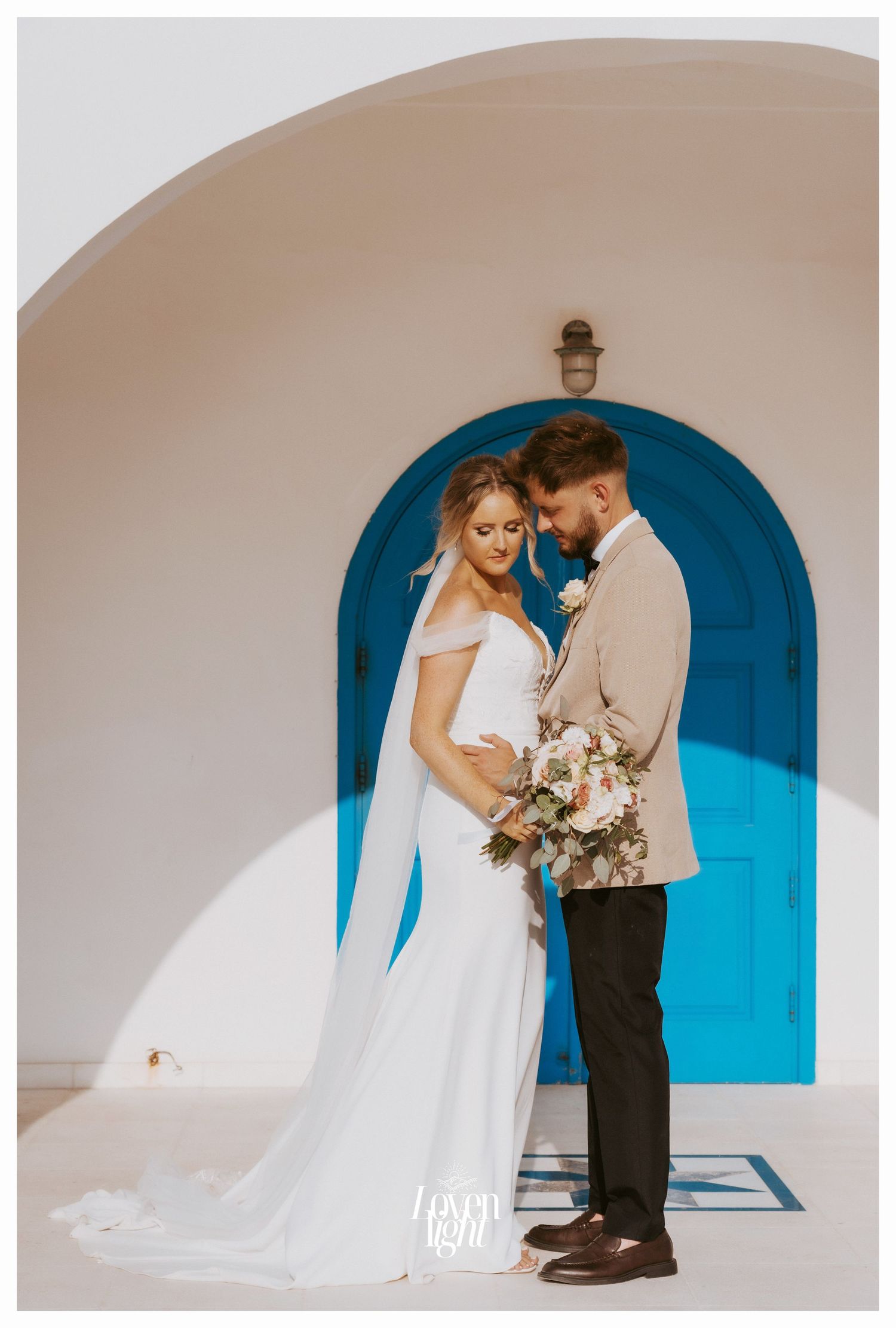 Intimate wedding moment captured under Mediterranean-style archway with turquoise blue door backdrop.