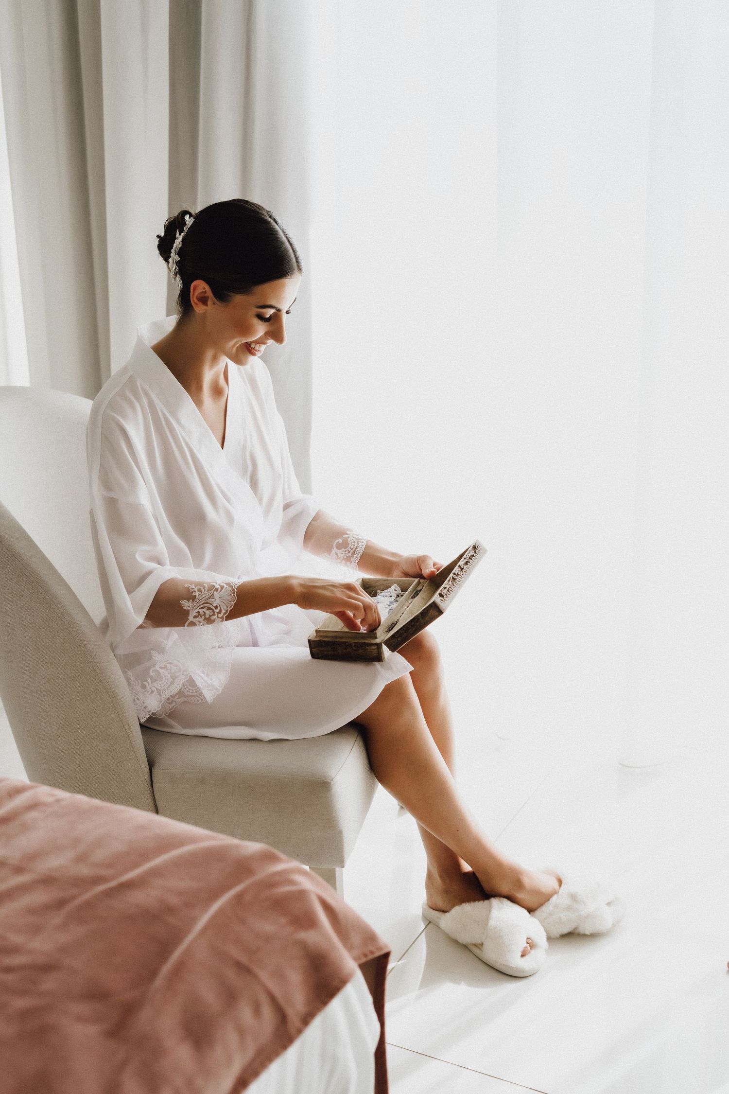 Woman in white robe and slippers sits in chair looking at mobile device.