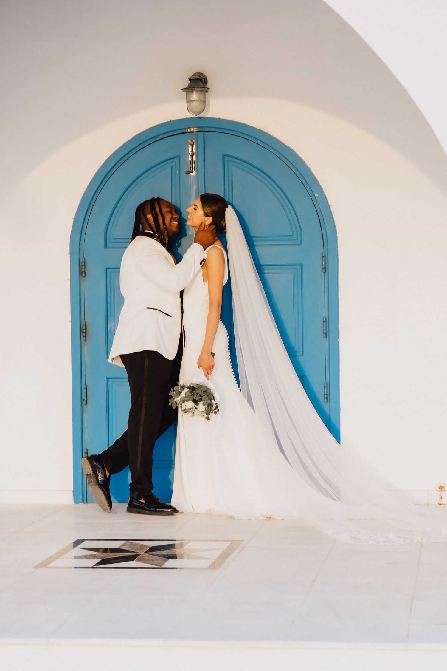 A romantic wedding couple poses against a bright turquoise door in a Mediterranean-style archway.