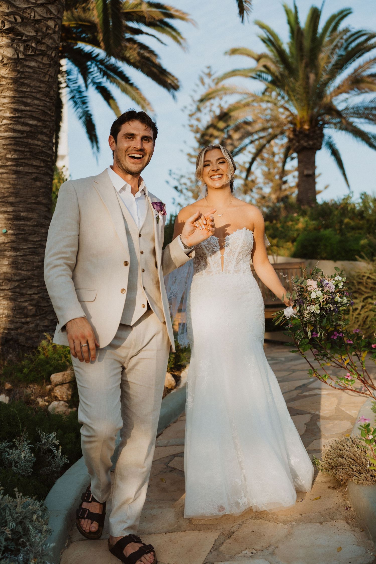 Joyful wedding couple laughing together on a Mediterranean garden pathway.