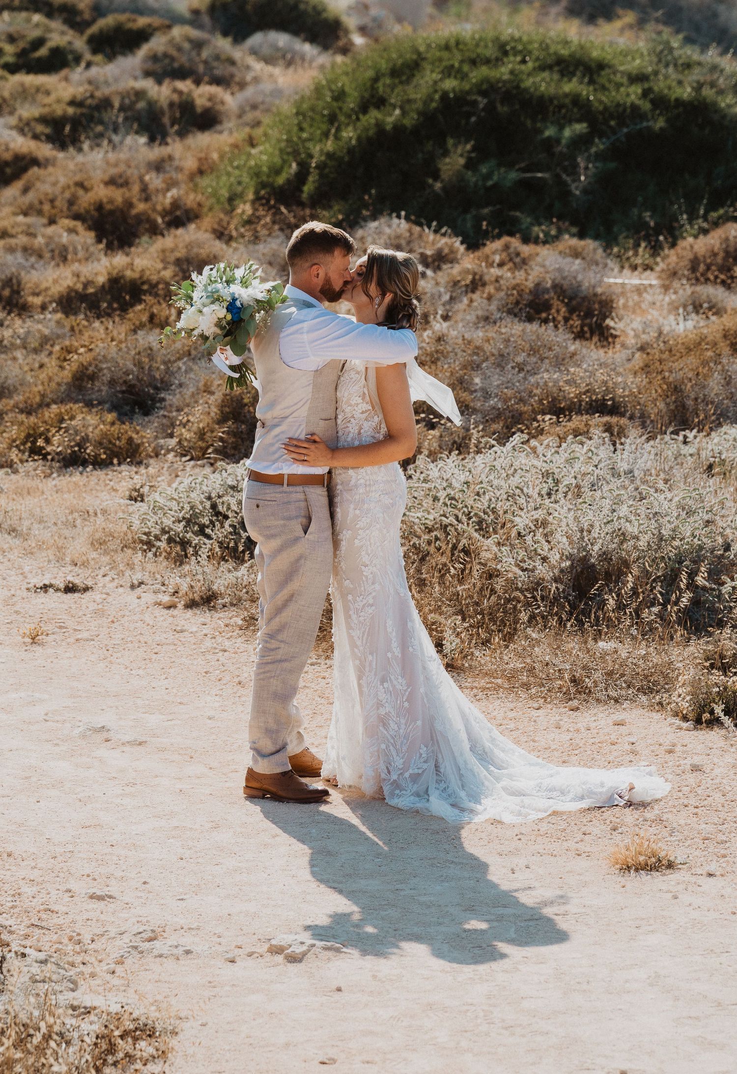Couple in wedding attire walking together on a desert path with mountains in background.