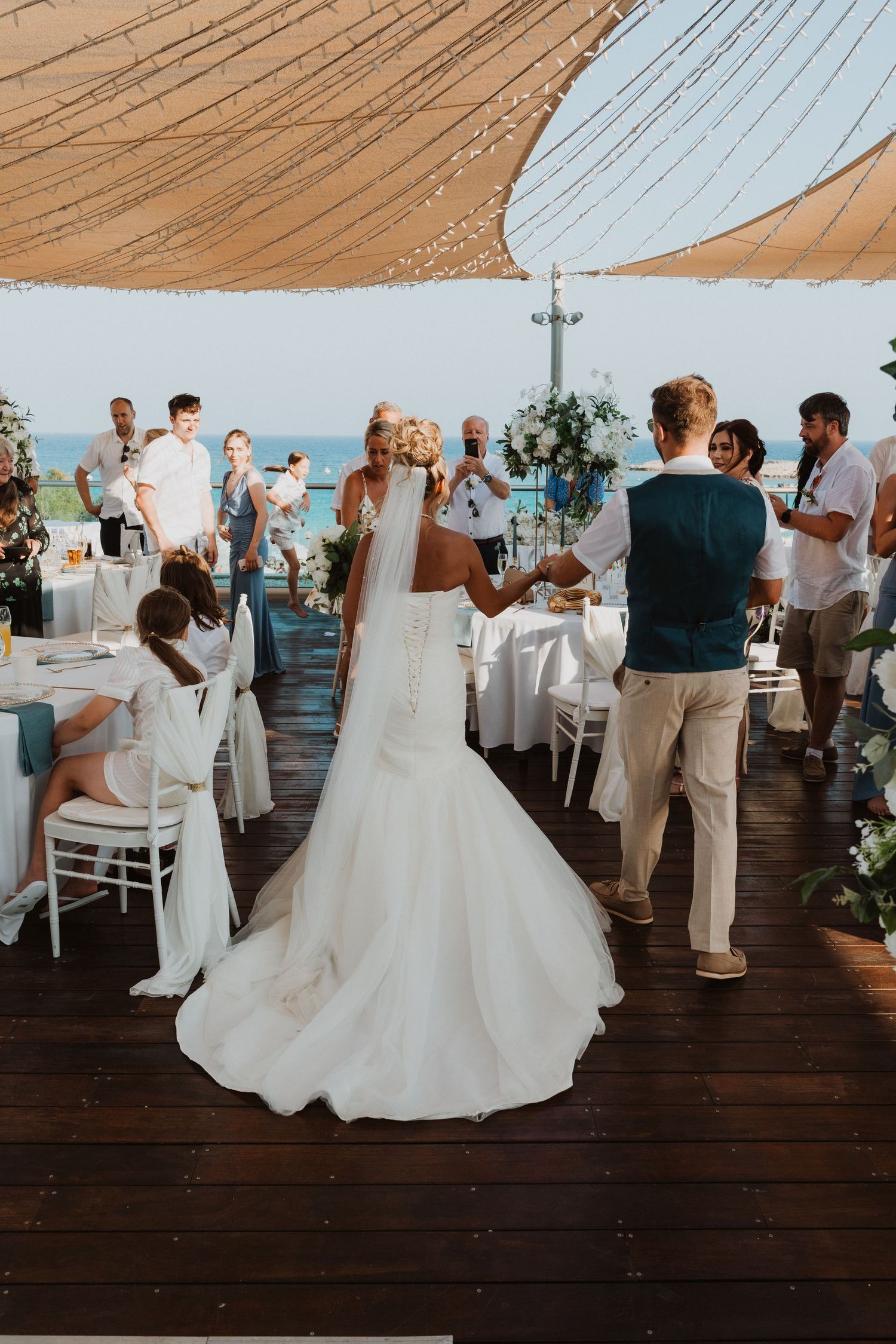 Bride and groom share first dance at elegant outdoor beach wedding reception under draped canopy with ocean view.