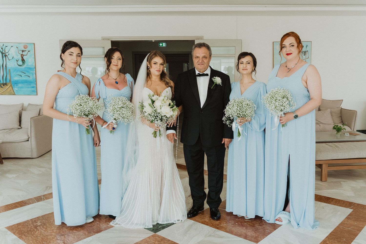 Bride with bridesmaids in blue dresses and father in tuxedo posing before the wedding.