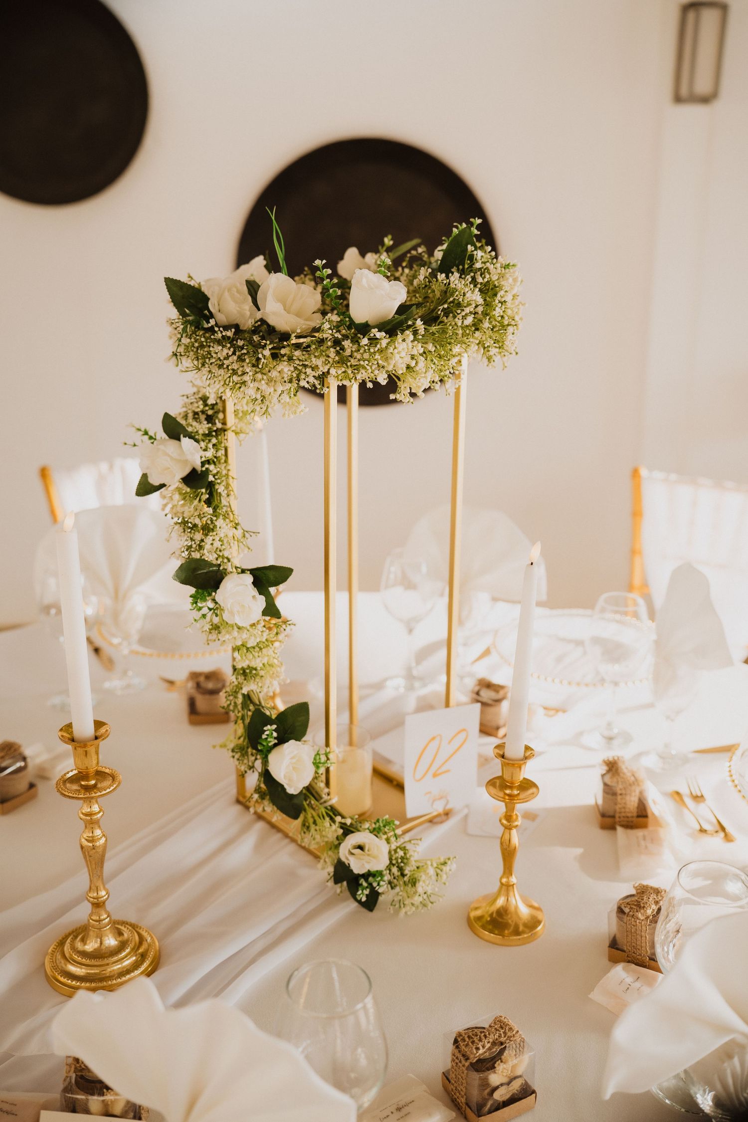 Elegant wedding reception table with tall gold floral centerpiece featuring white roses and greenery with gold candlesticks.