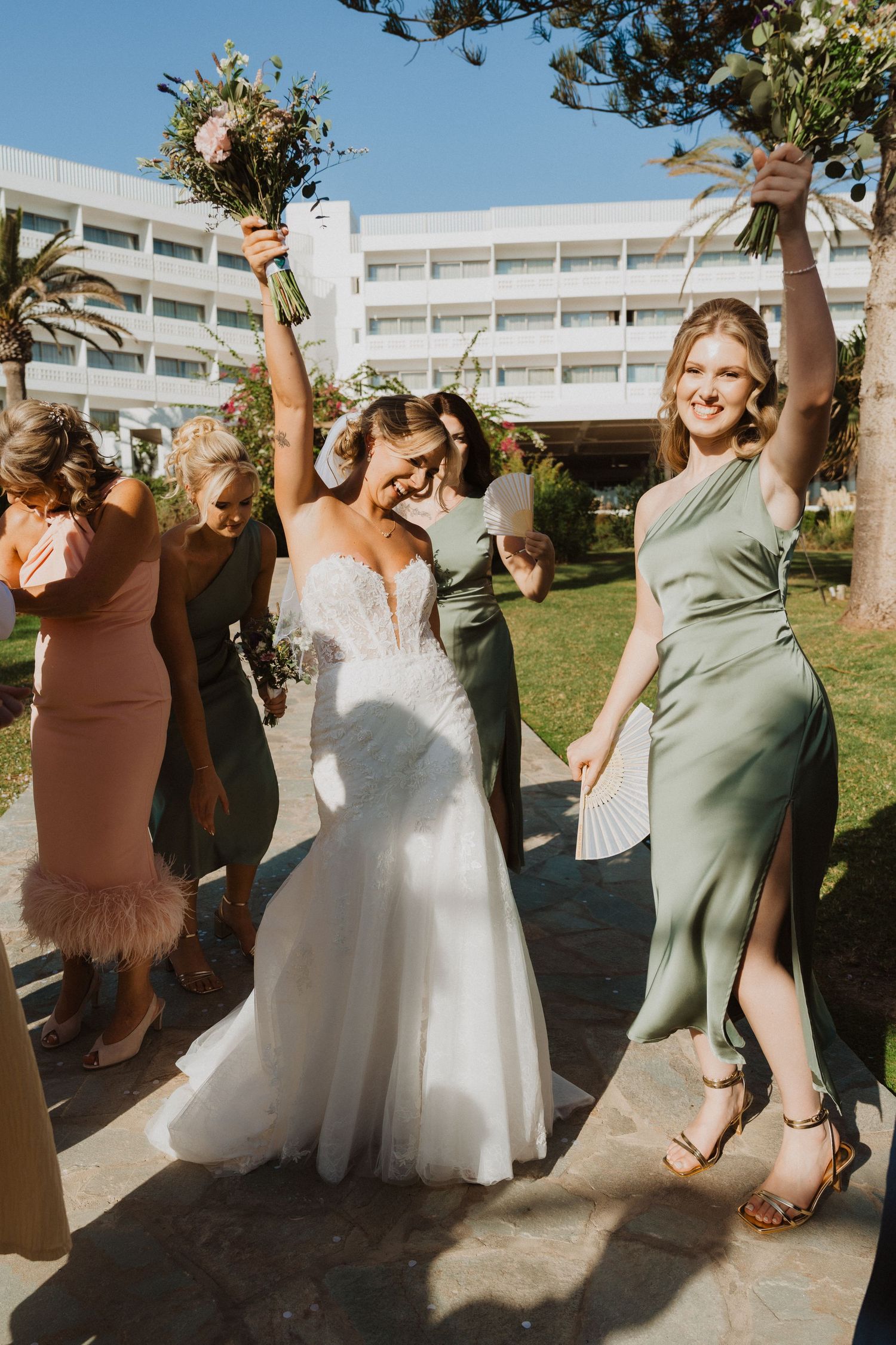 Bridesmaids in sage green dresses dancing and celebrating with the bride at an outdoor wedding.