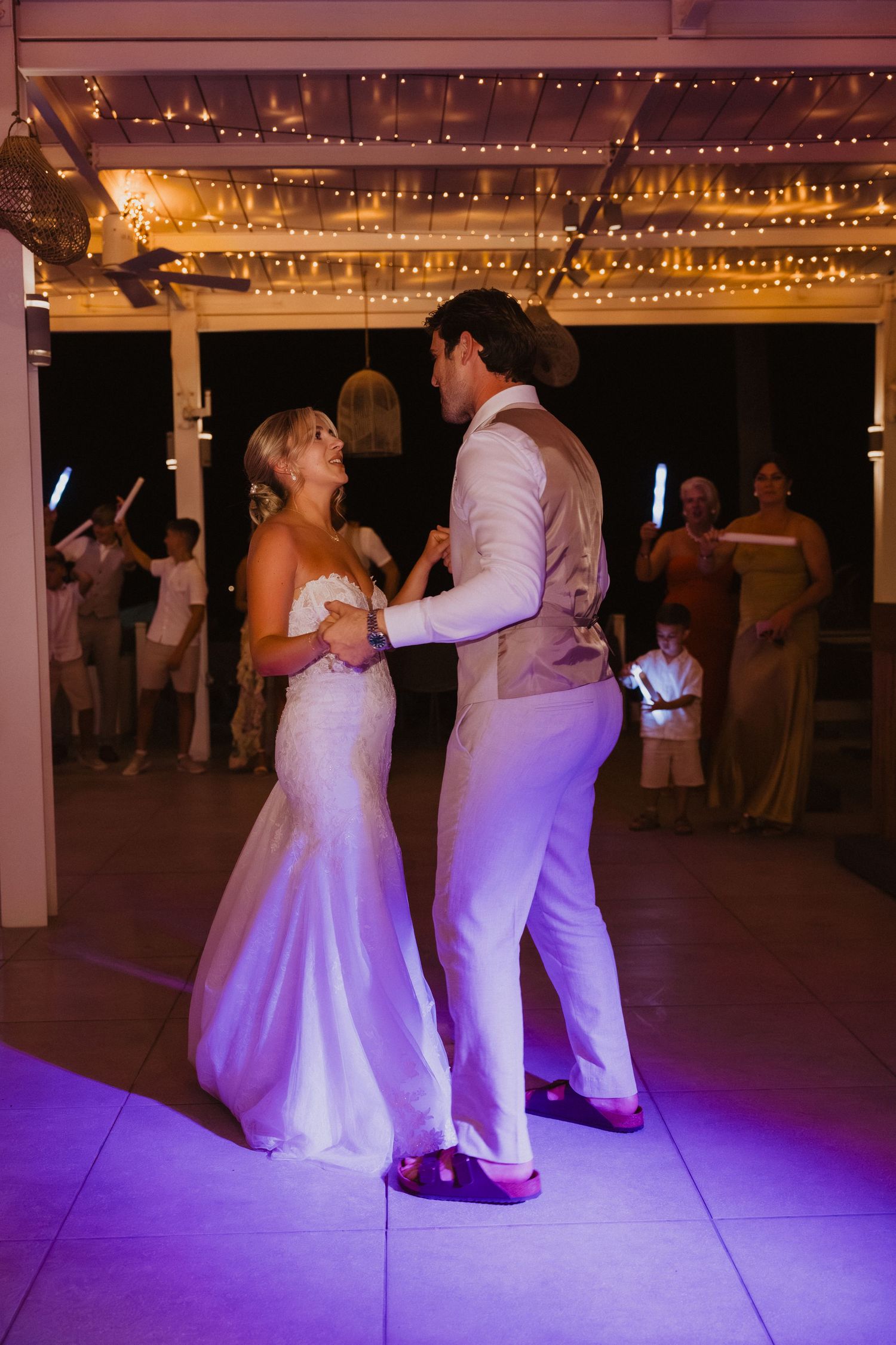 Couples dancing at wedding reception under string lights with purple floor lighting.