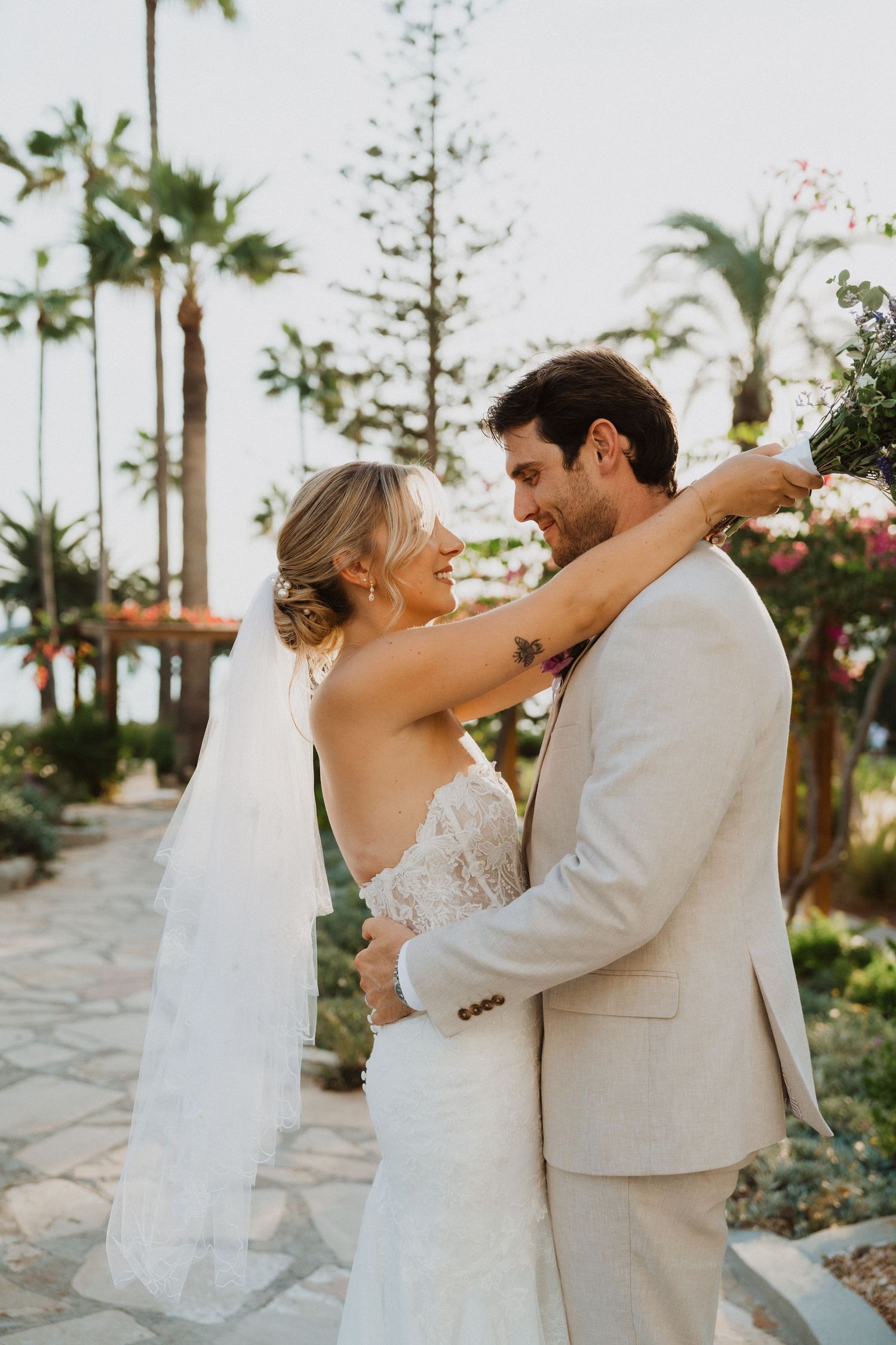 Couple embraces on a stone pathway surrounded by tropical landscaping.