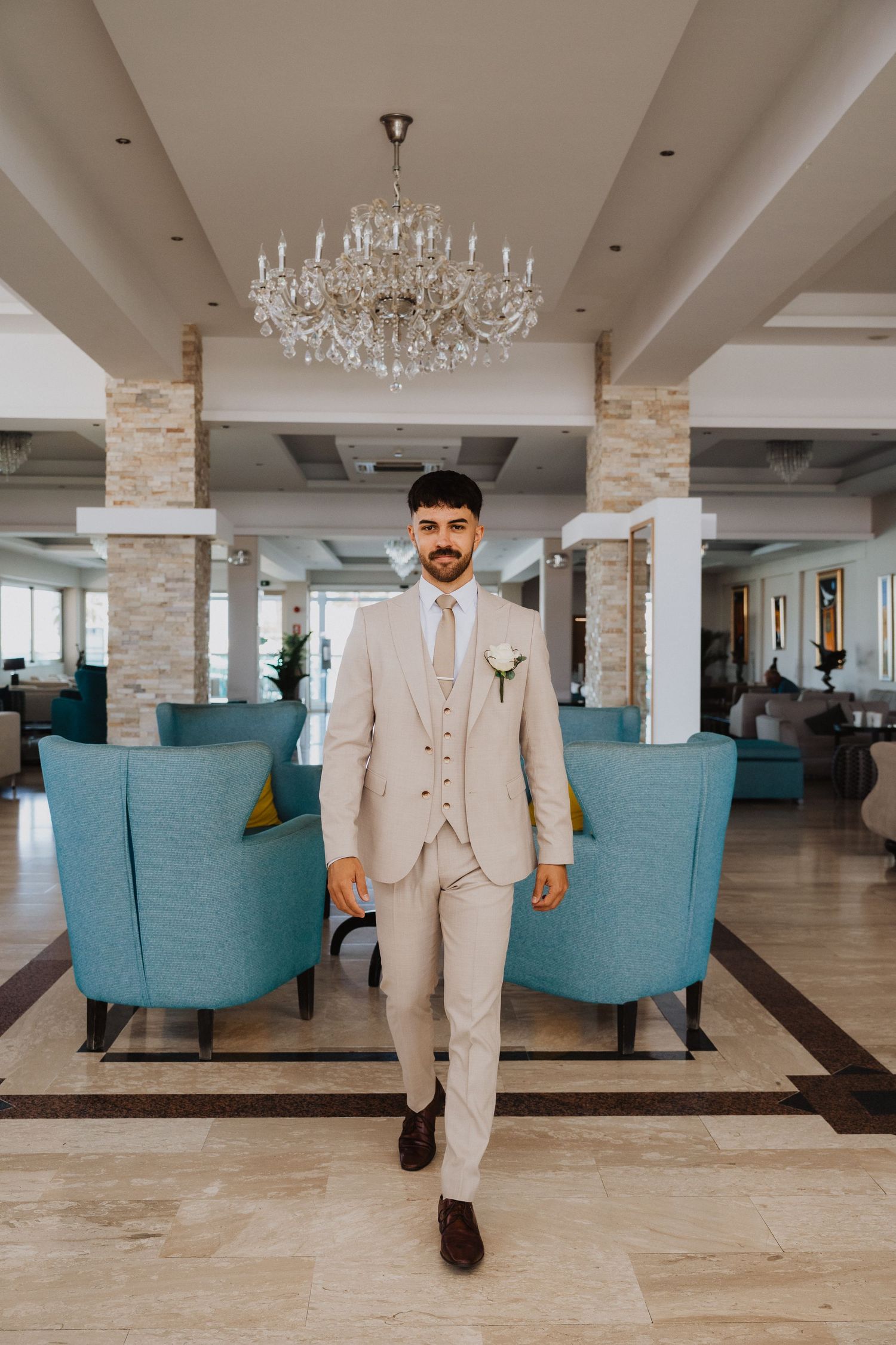 A light colored suit is displayed in a spacious venue with teal furniture and stone accents.