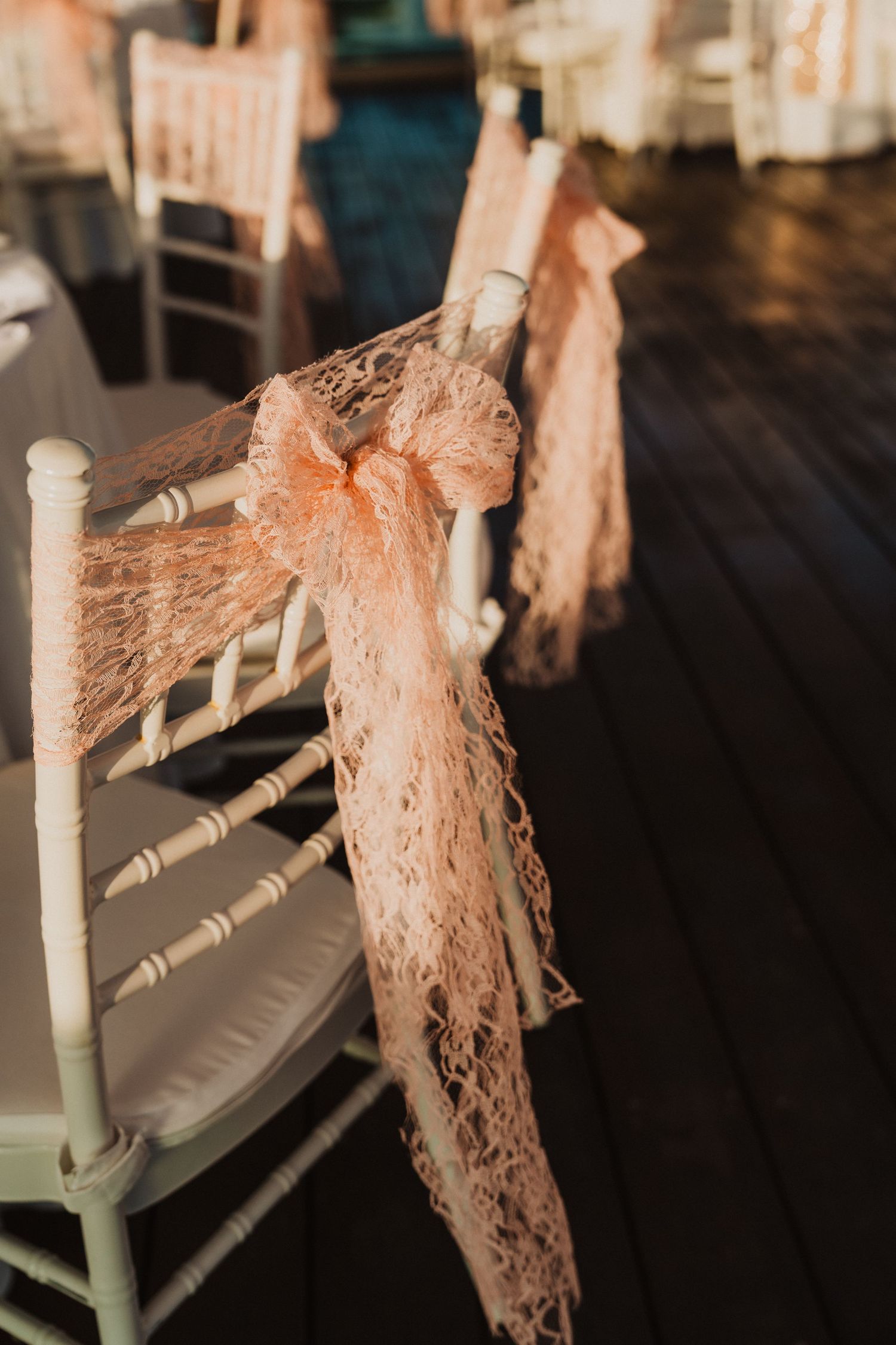 White chairs decorated with delicate peach lace bows for a wedding ceremony.