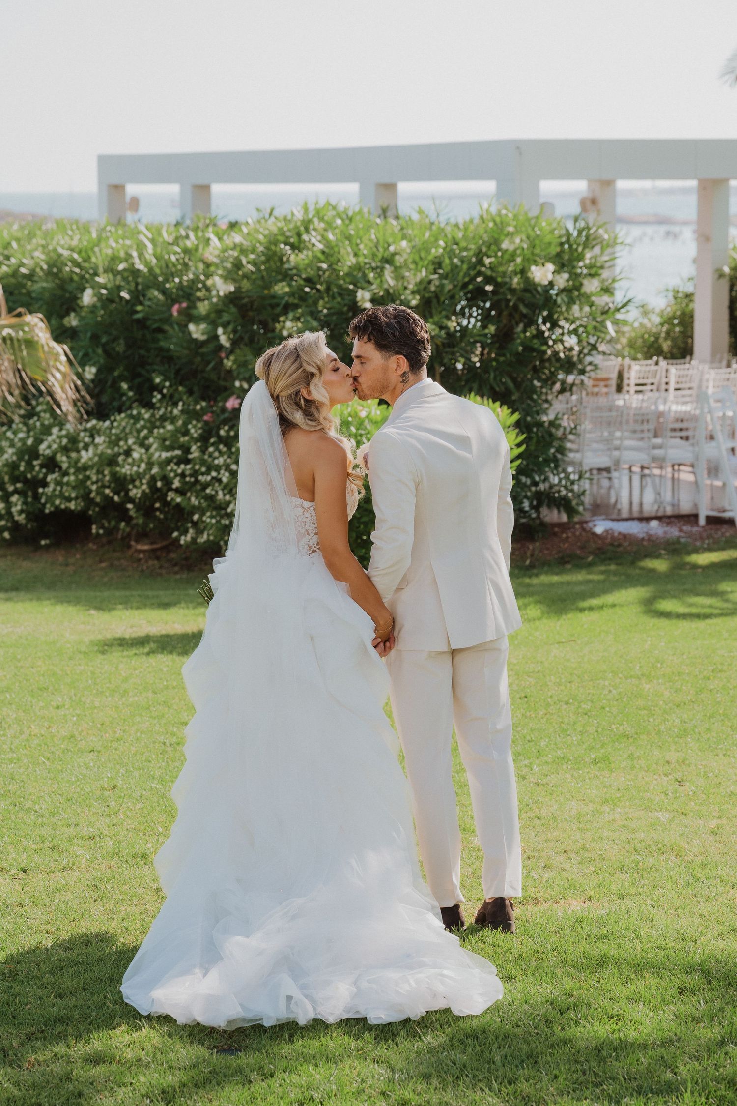 A romantic outdoor wedding scene with a couple in white sharing a tender moment on a lush green lawn.